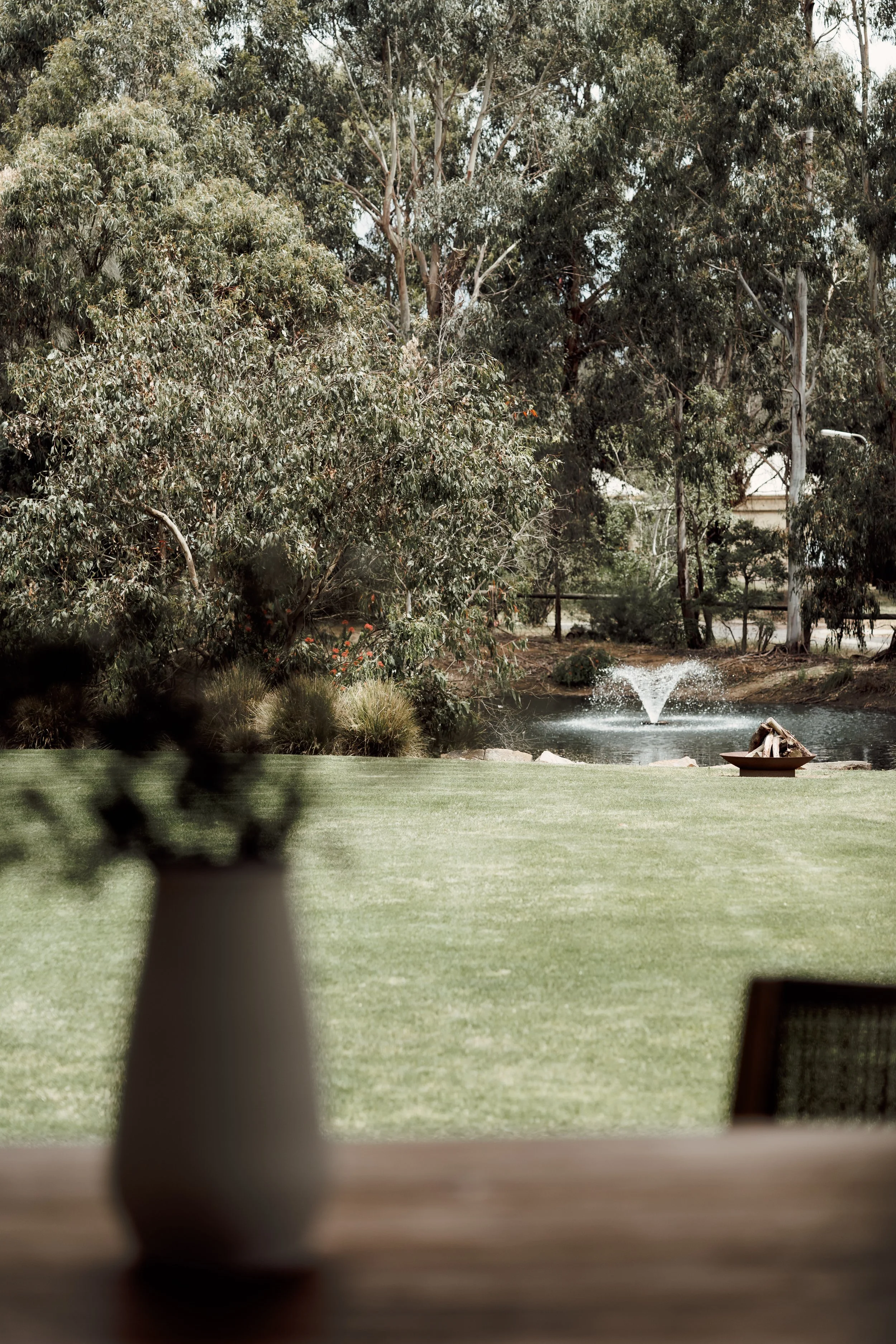 A backyard scene with a water fountain, a grassy lawn, and trees in the background.