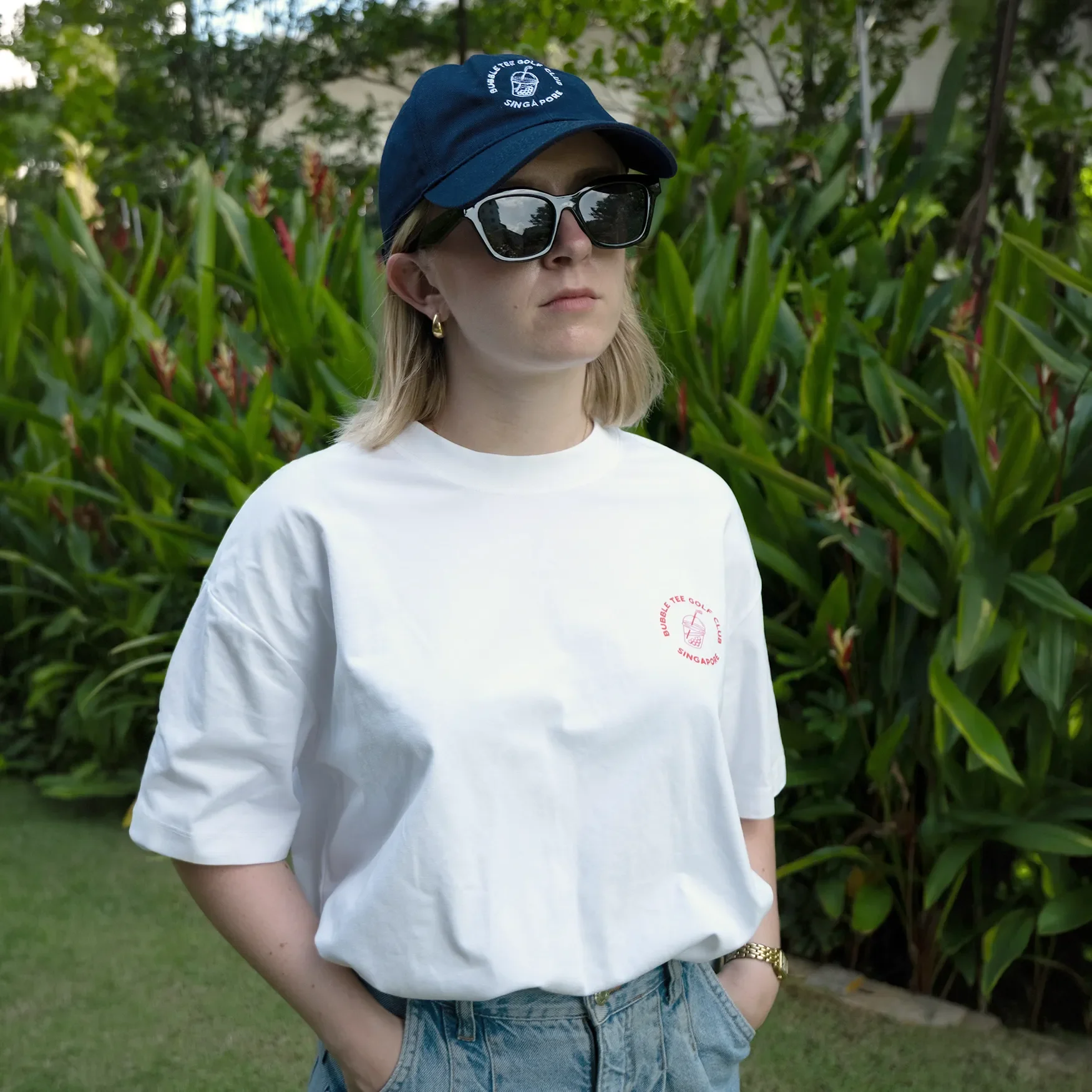 Female golfer wearing white Bubble Tee Golf Club t-shirt with small front logo and large back logo print, standing on Singapore golf course, relaxed premium golf apparel.