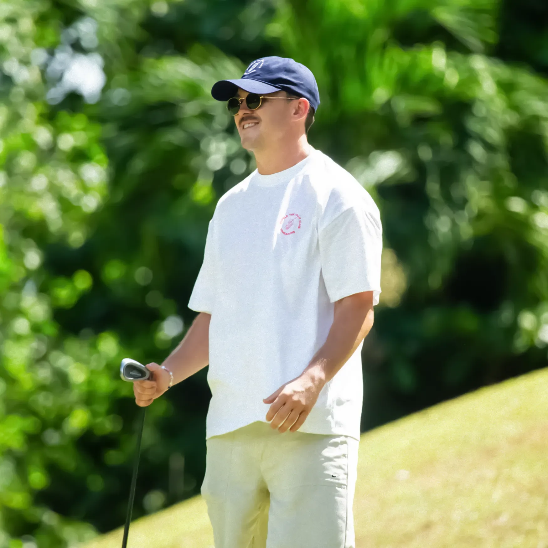 Male golfer wearing a white Bubble Tee Golf Club t-shirt with minimalist front logo detail, styled for warm-weather golf in Singapore, relaxed premium streetwear influence.