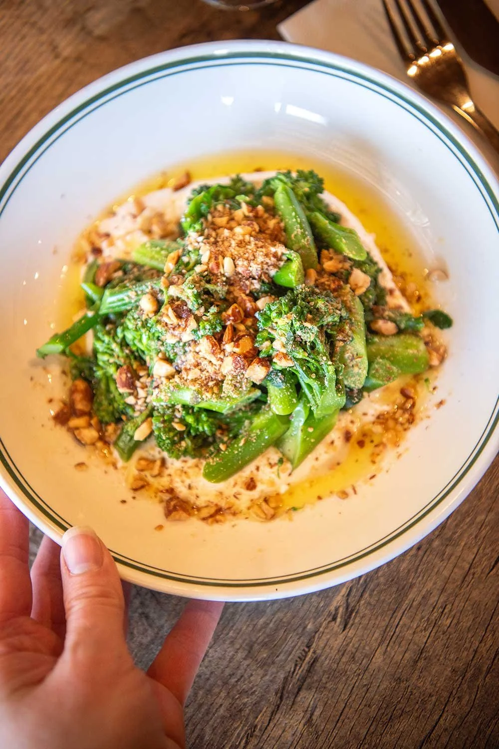 A curry dish with broccoli, topped with chopped nuts, grated cheese and seasoning on a wooden table.