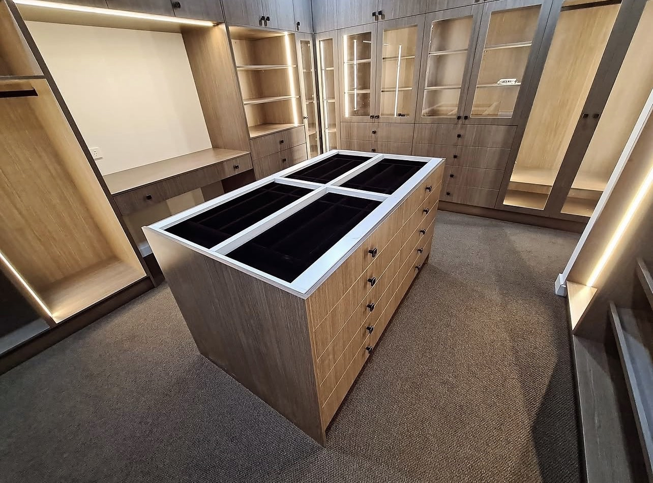 Empty walk-in closet with built-in wooden cabinets and an island in the center with glass display cases.