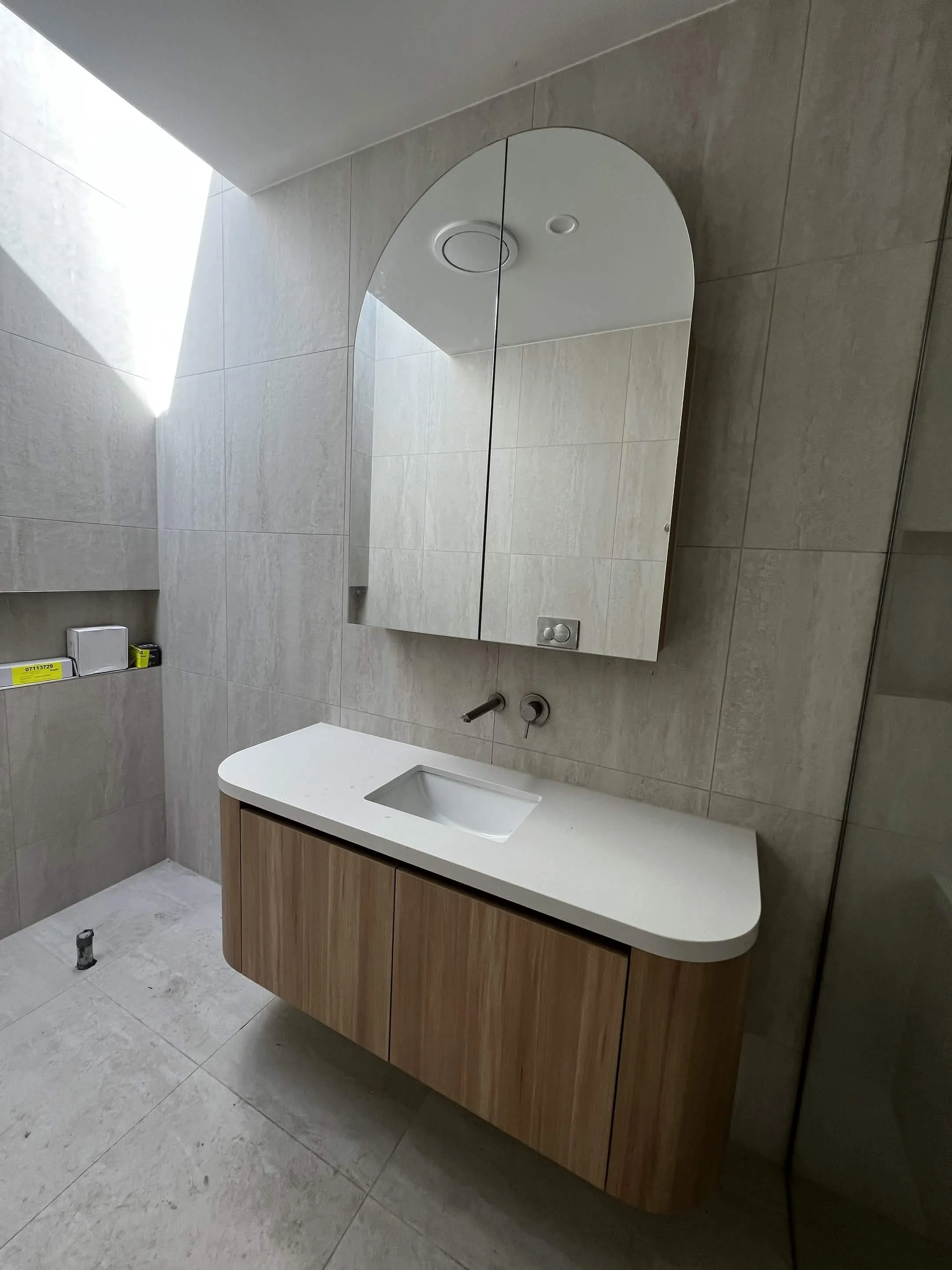 Modern bathroom with beige tiled walls and floor, a white vanity with an integrated sink, a mirrored cabinet, and a ceiling light fixture.