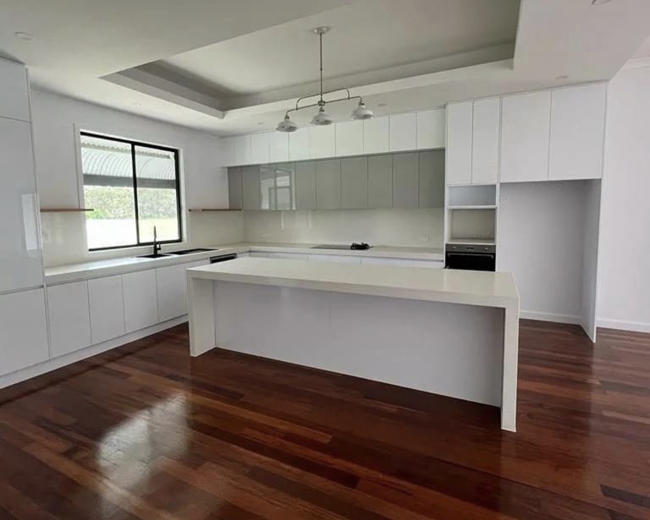 Modern kitchen with white cabinetry, a large central island, wood flooring, and a window over the sink.