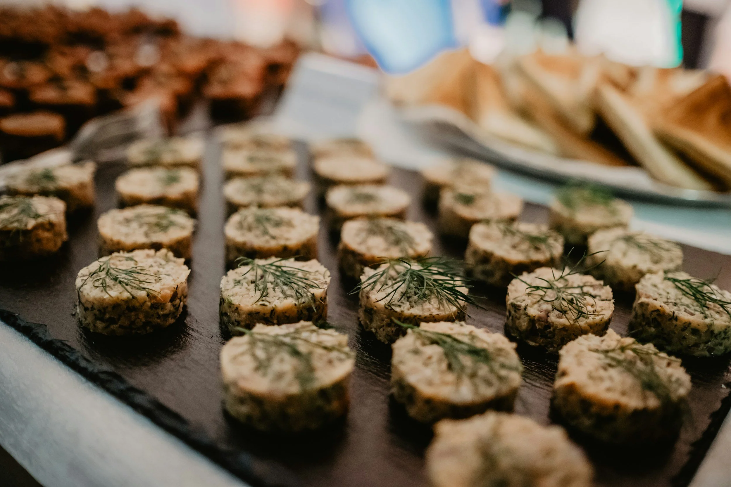 Close-up of round crackers topped with cream cheese and garnished with fresh dill, arranged on a black platter.