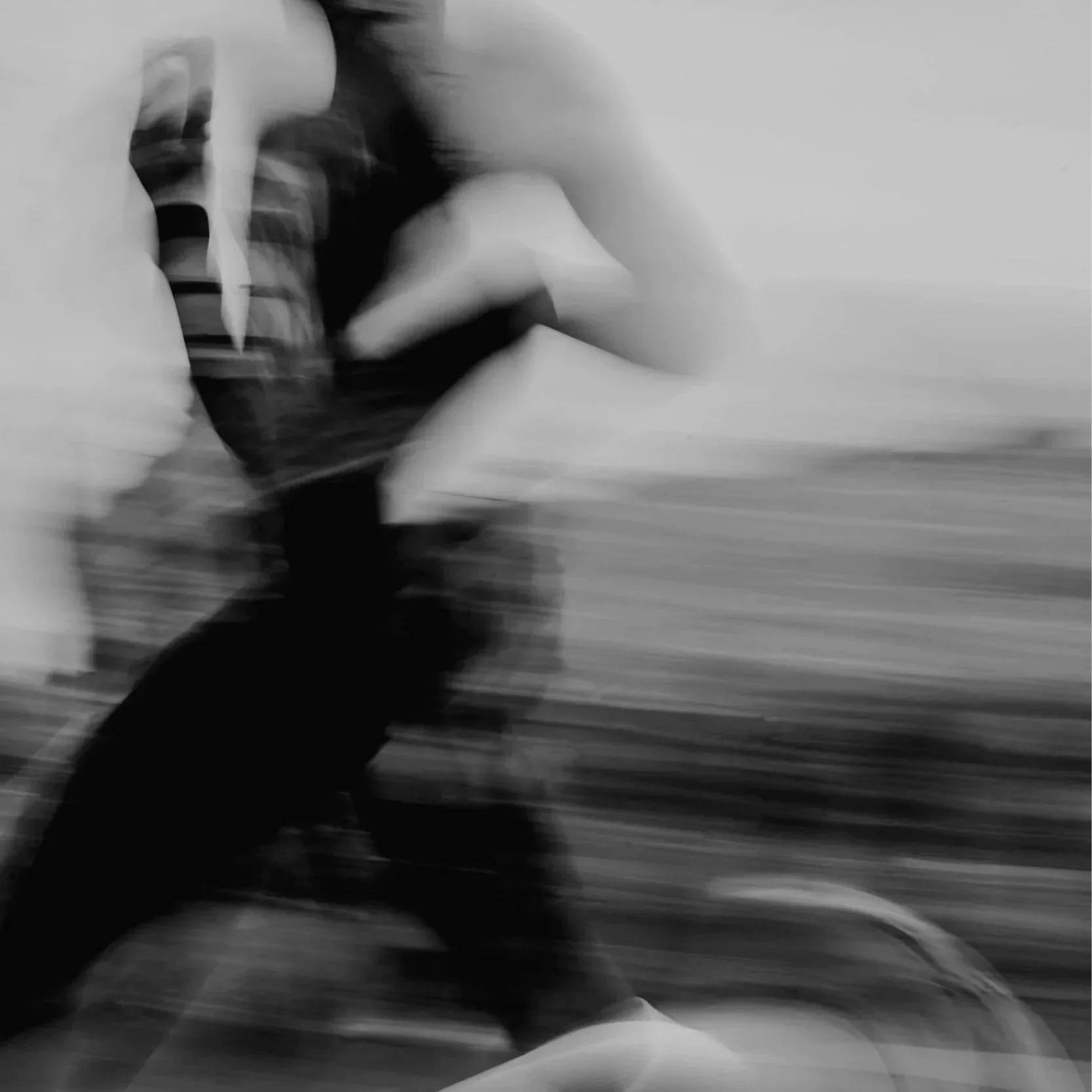 A blurry black and white photo of a person in a hoodie, kneeling on the ground with their head down and hands on their knees, against a plain background.