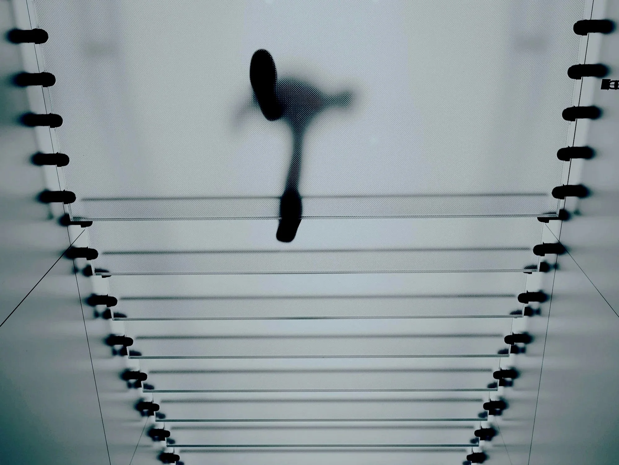 Looking up at a ceiling with evenly spaced black light fixtures and a textured white surface. A shadowy object casts a black silhouette on the ceiling.