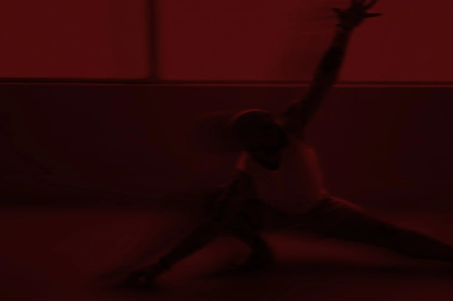 A person squatting and holding onto a chain attached to the ceiling in a dark, red-tinted environment.
