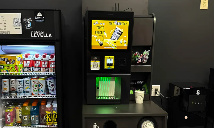 Distributeur automatique de boissons énergisantes avec écran numérique, situé à côté d'un autre distributeur contenant des boissons en bouteilles.