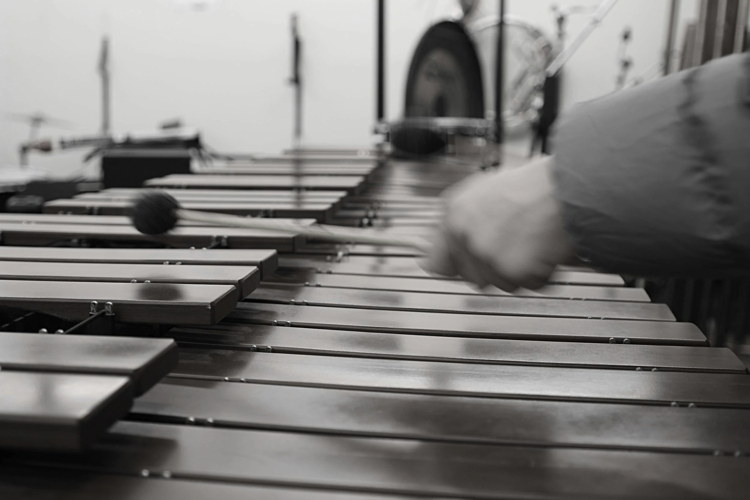 Close-up of a keyboard instrument with metal strings being played by a hand in a blurry black-and-white photograph.