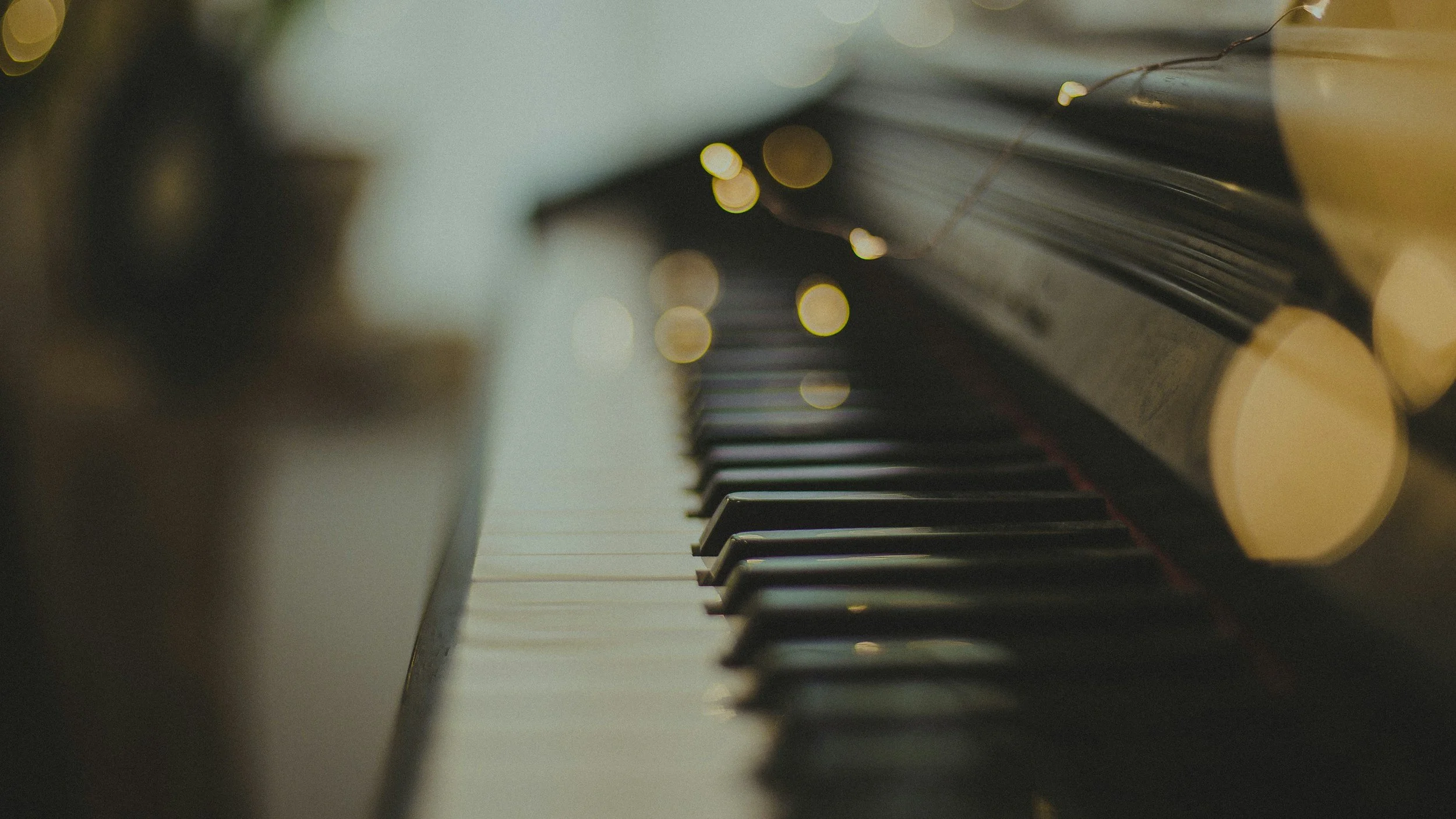 Close-up of a piano keyboard with some yellow piano keys visible and blurry lights in the background.