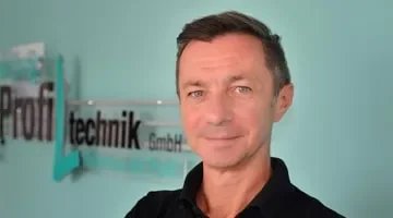 Ein Mann steht vor einem Firmenlogo mit den Worten 'technik GmbH' auf einer Wand.