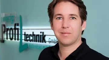 Porträt eines Mannes vor einer Firmenbeschilderung, die 'Profit Technik GmbH' zeigt.