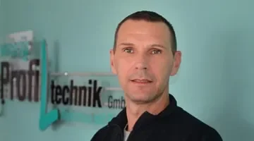 Ein Mann steht vor einer Wand mit einem Firmenlogo, das 'Profi Technik GmbH' heißt.