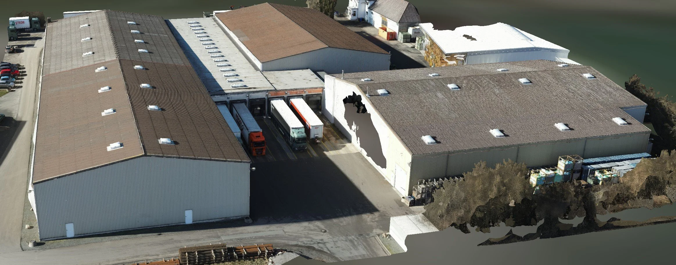 Lagerhalle mit mehreren LKWs, Parkplätzen und einem Wasserteich im Hintergrund.