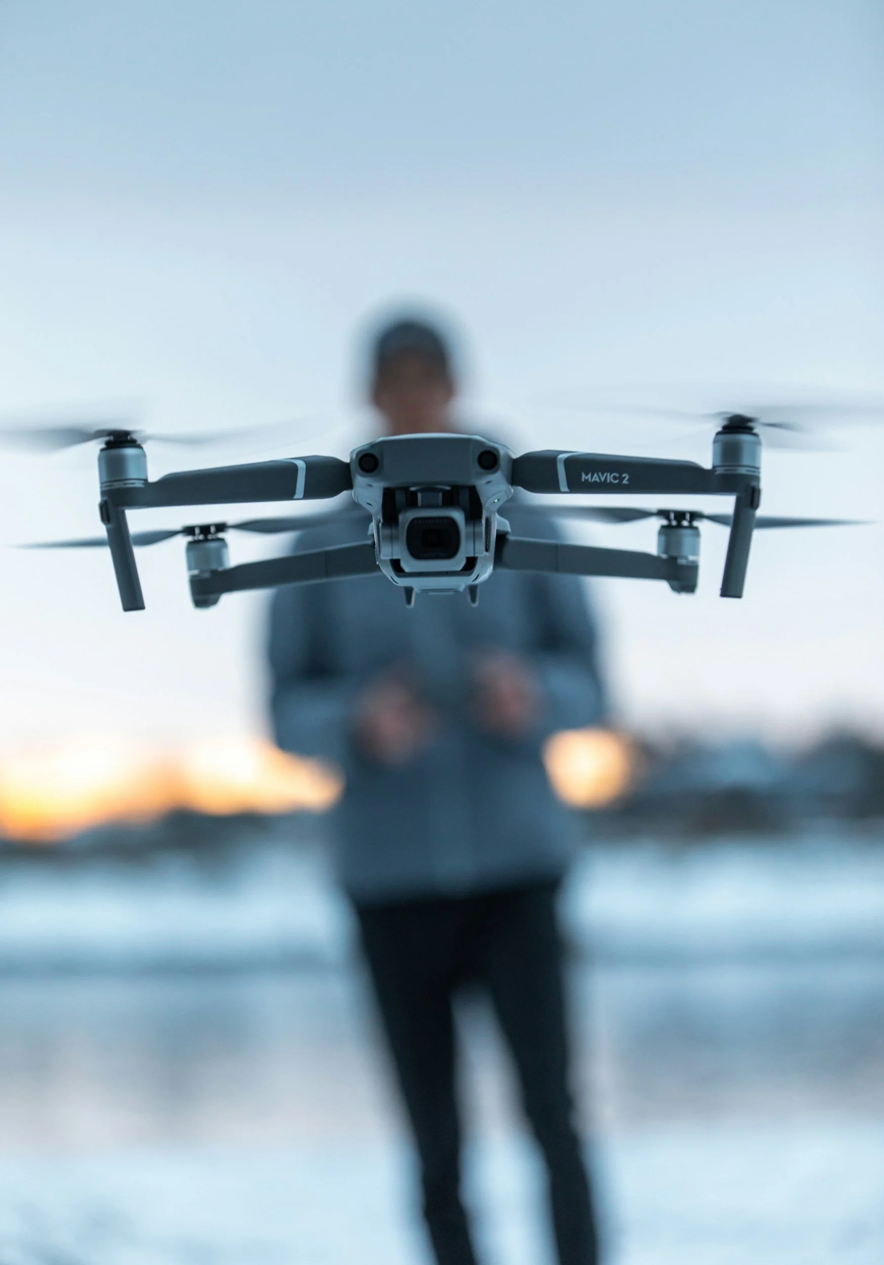 Un drone volant avec un homme flou au fond pendant le coucher du soleil.
