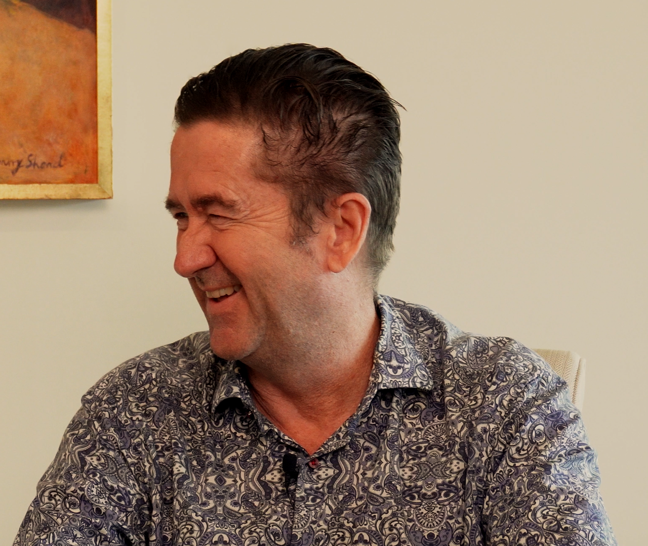 Dr Stephen Van Mil, co-host of this podcast, sits laughing and looking to the left.