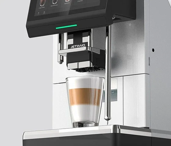 A Jetinno coffee machine brewing a layered latte in a glass placed on the drip tray.