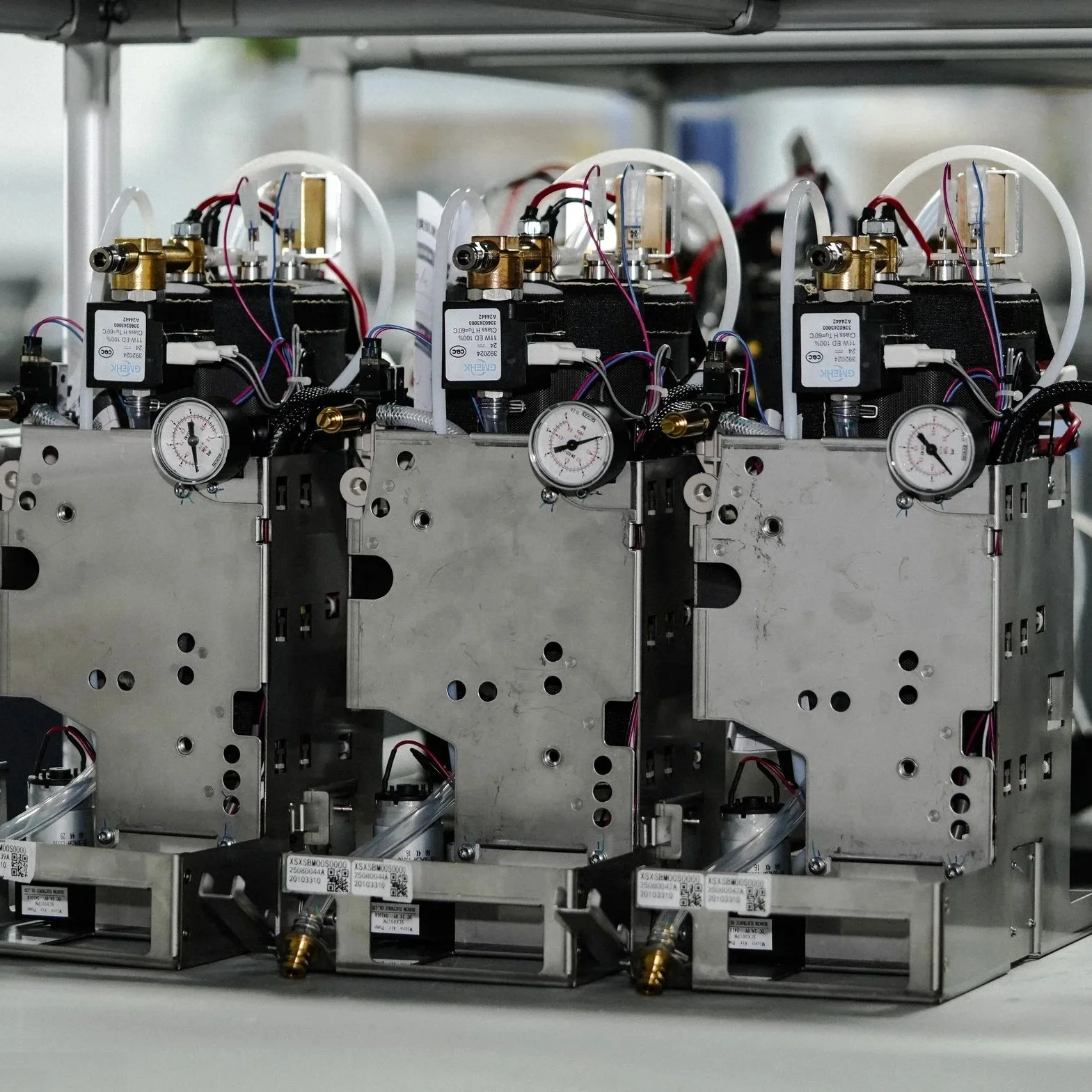 Internal mechanics of Caye coffee machine with gauges, wires, and brass fittings arranged on a metal frame on a conveyor belt.