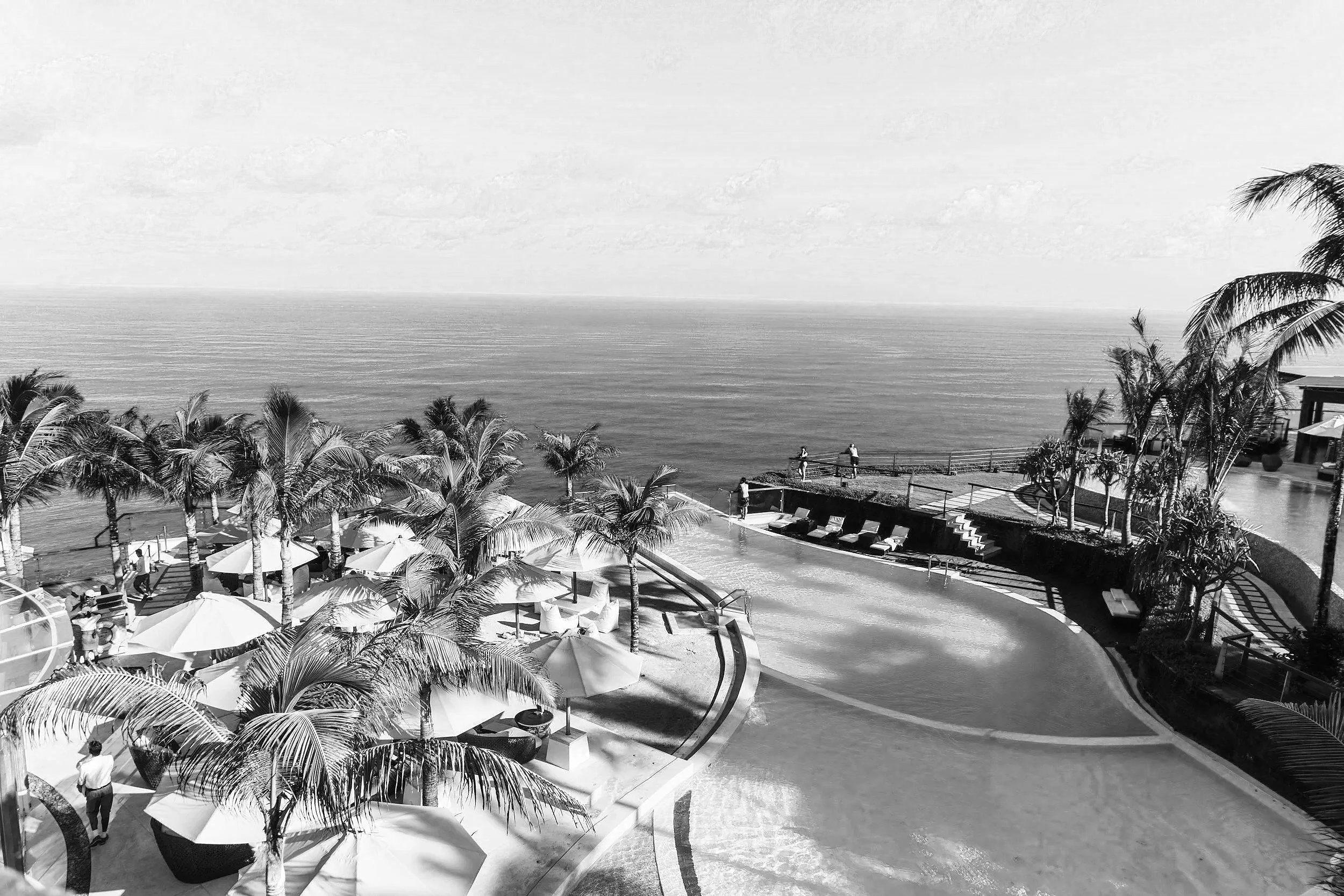 Une vue d'une plage luxueuse avec des palmiers, des parasols et des chaises longues, face à l'océan.
