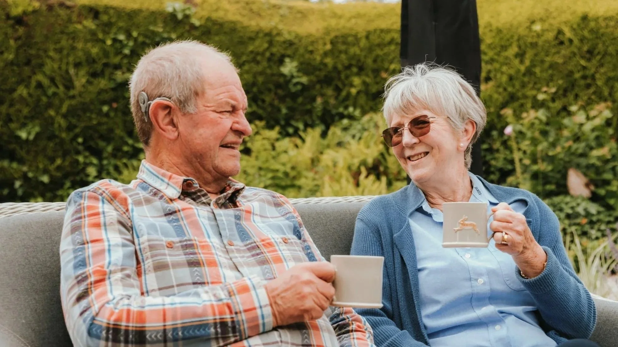 A happy couple sharing a laugh and a morning cup of coffee in their backyard garden.