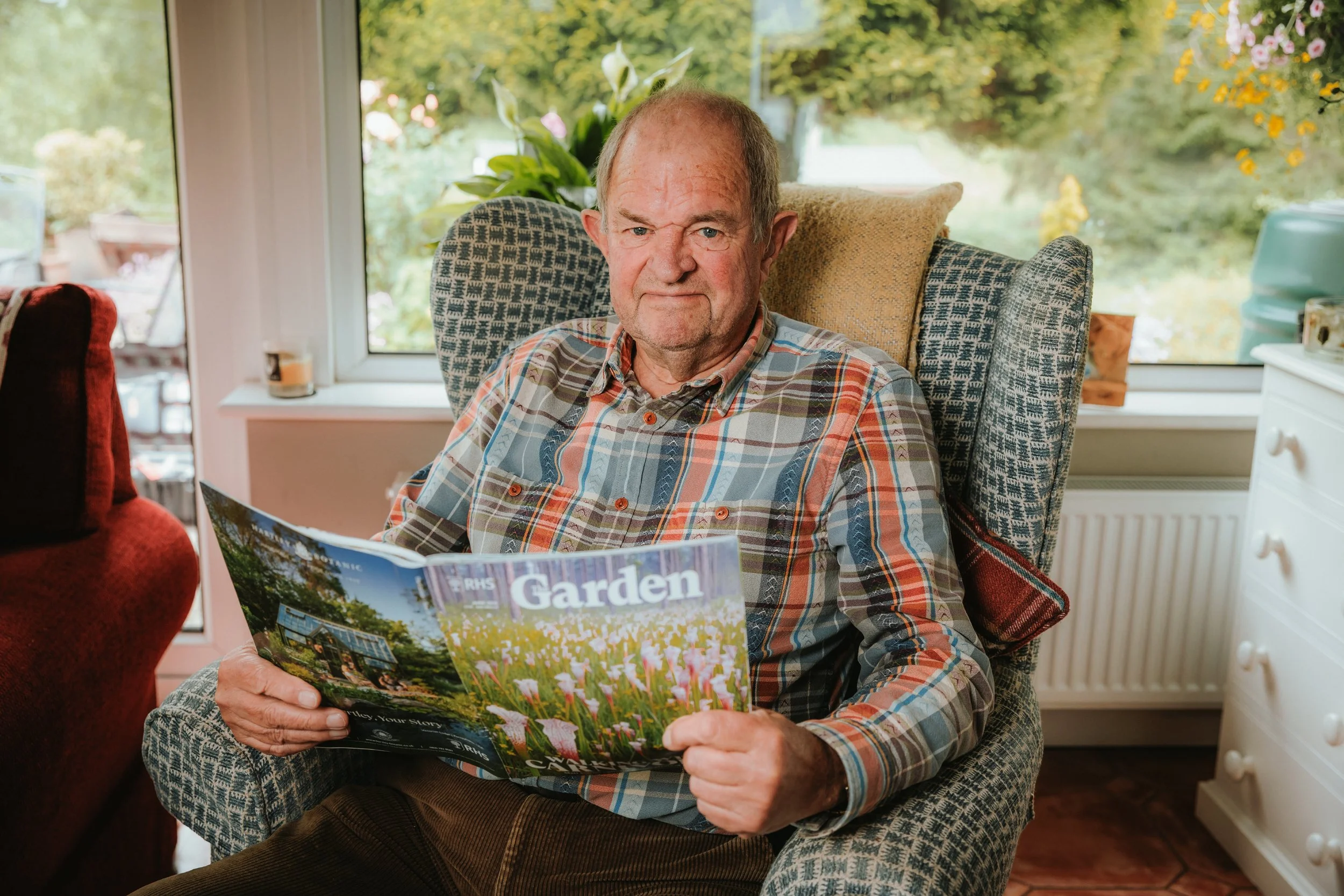 A man enjoying a peaceful time relaxing in an armchair at home while reading a gardening magazine.