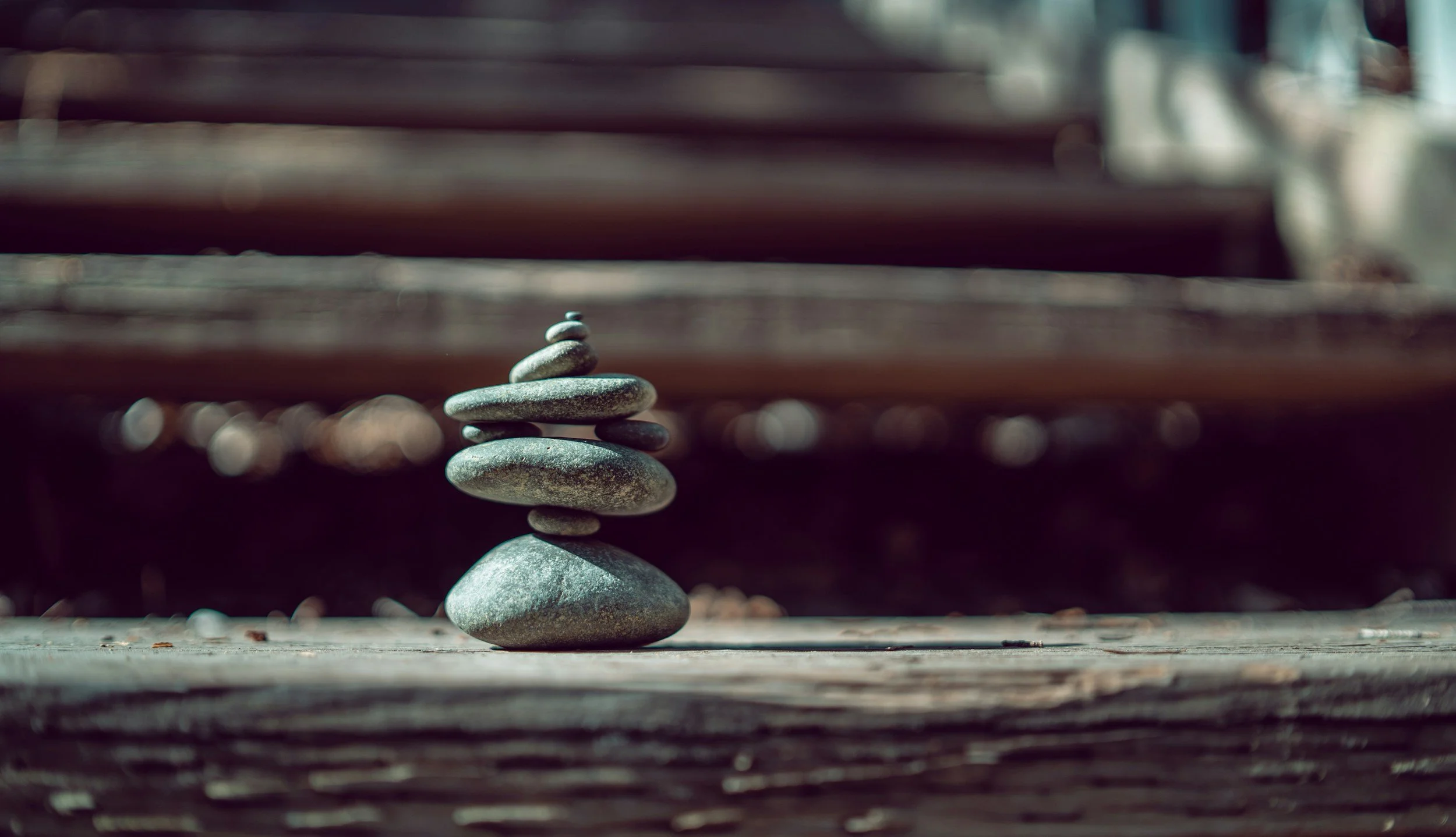 Stacked smooth stones on a wooden surface with blurred stairs in the background.