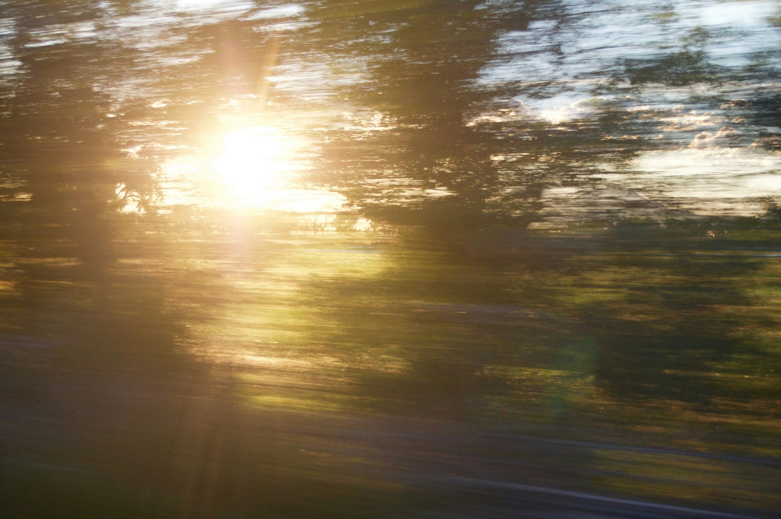 Blurred photo of a sunrise or sunset reflecting on water with trees visible in the background