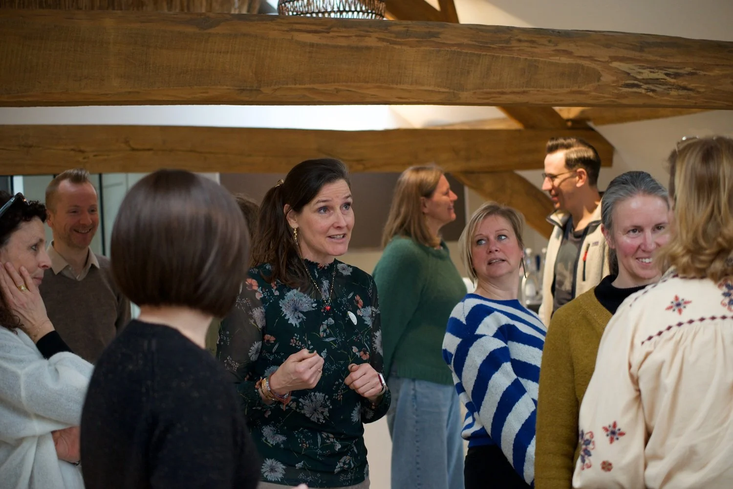 Group of people engaged in conversation indoors with wooden beams and warm lighting