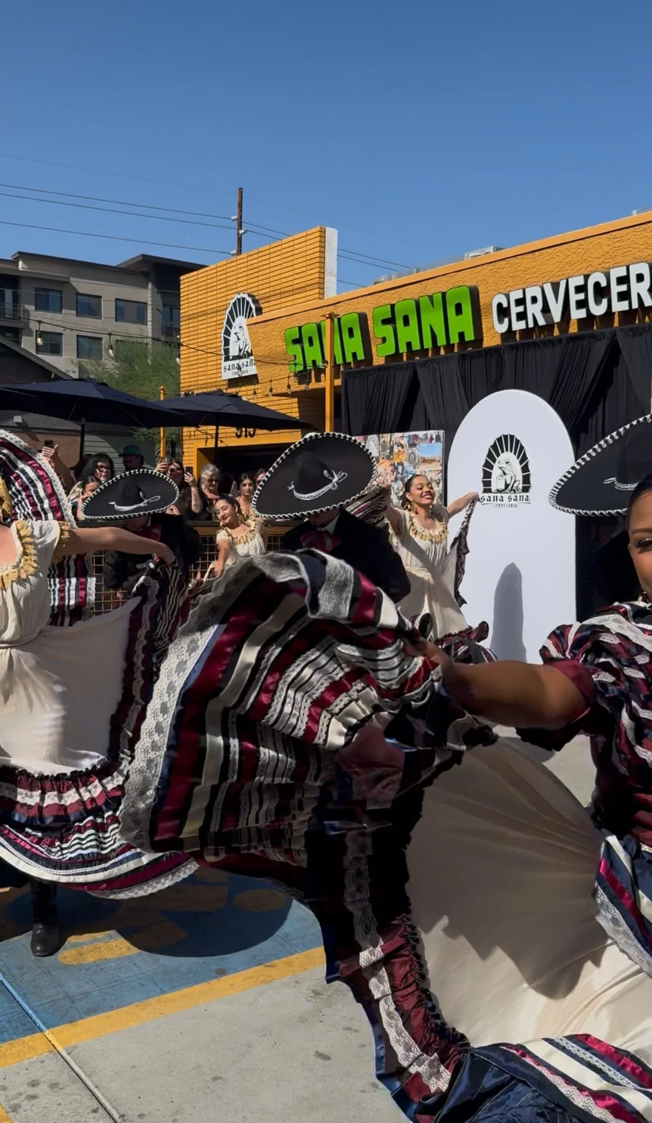 Mexican dancers wearing traditional colorful costumes perform in front of a crowd during a cultural event.