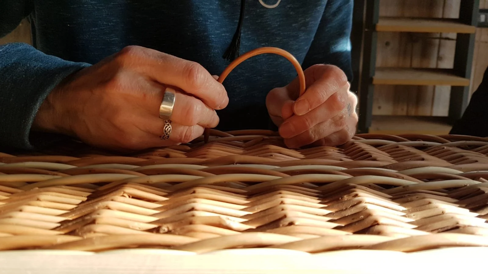 Close-up of a person's hands weaving a wicker coffin using wicker strips on a table.