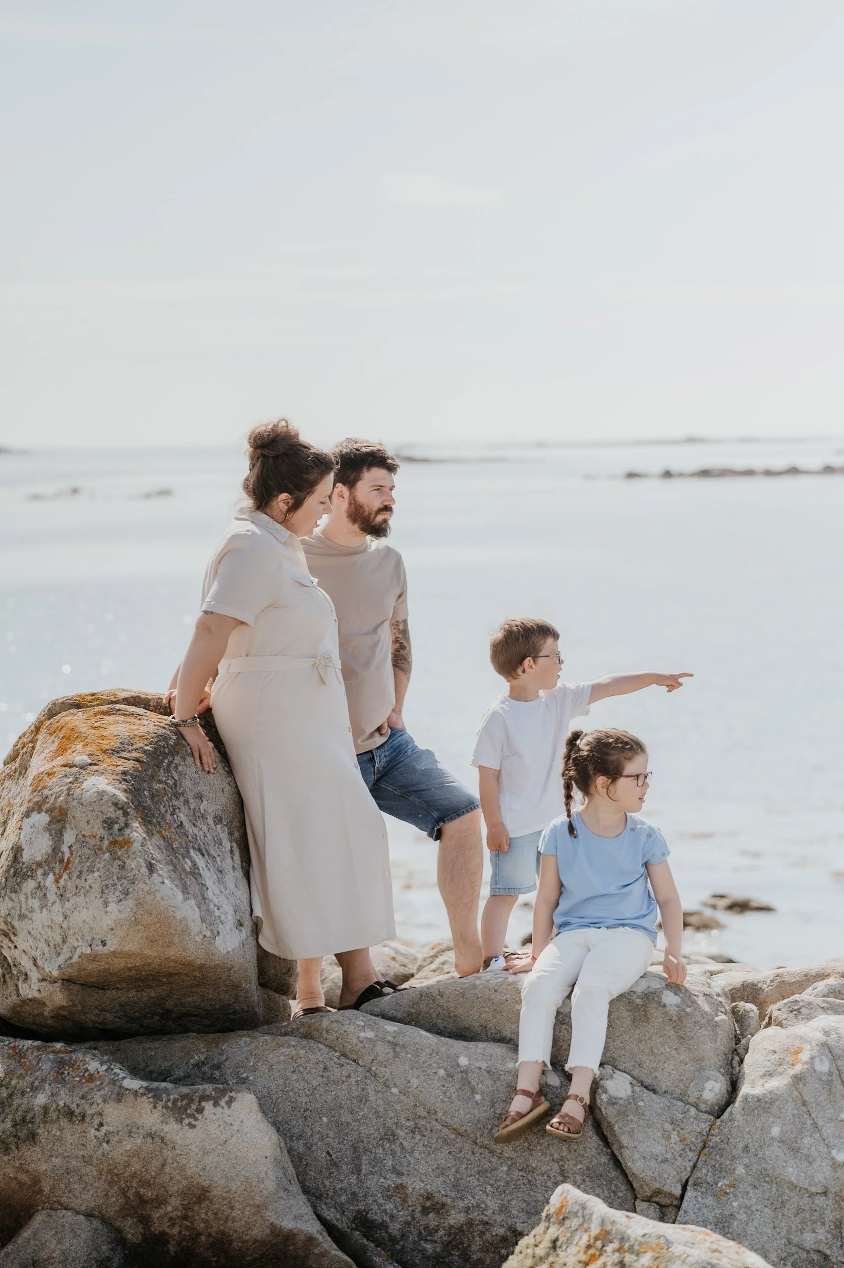 Famille de cinq personnes sur des rochers près de la mer, regardant et pointant vers l'océan, fond de ciel clair et mer calme.