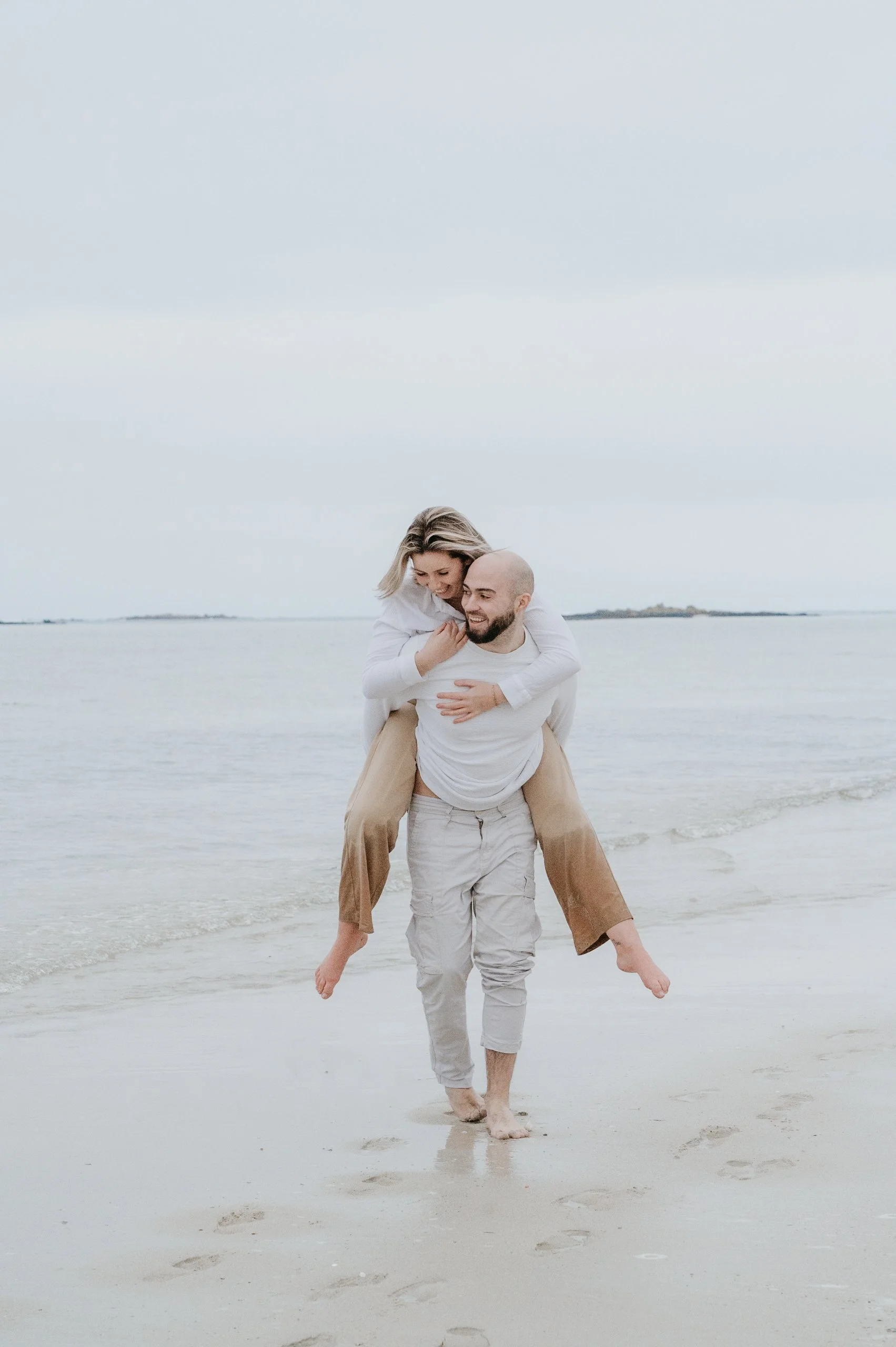 Un couple heureux à la plage, l'homme portant la femme sur ses épaules, marcher dans le sable avec la mer en arrière-plan.