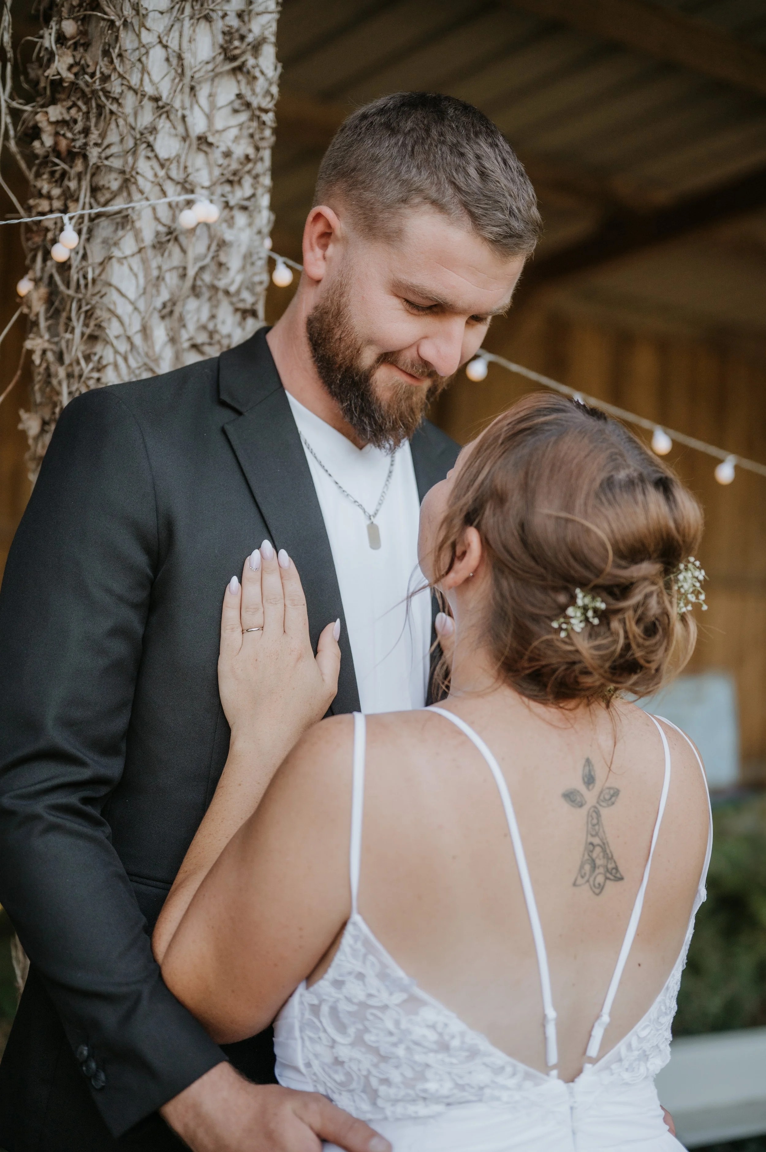Un couple danse lors de leur mariage, l'homme porte une veste noire et la femme porte une robe blanche à bretelles, elle a un tatouage dans le dos et des fleurs dans ses cheveux.
