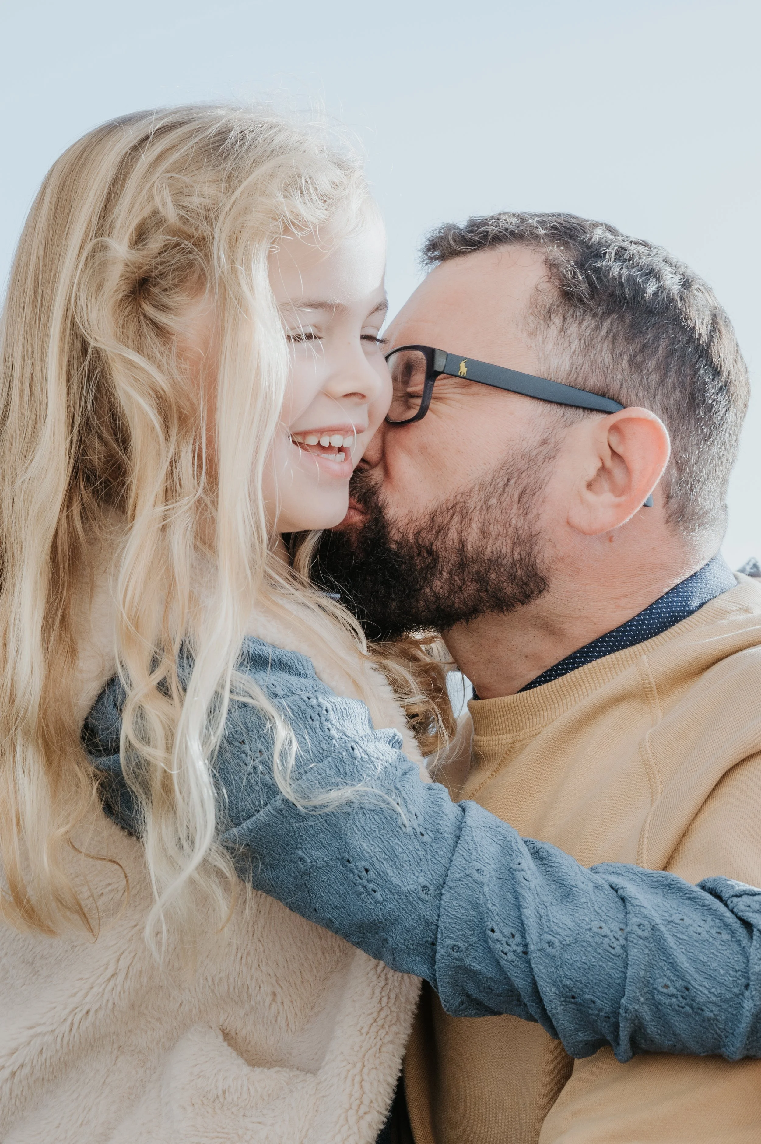 Un homme et une jeune fille se donnent un bisou en sourire, dans un éclairage naturel.