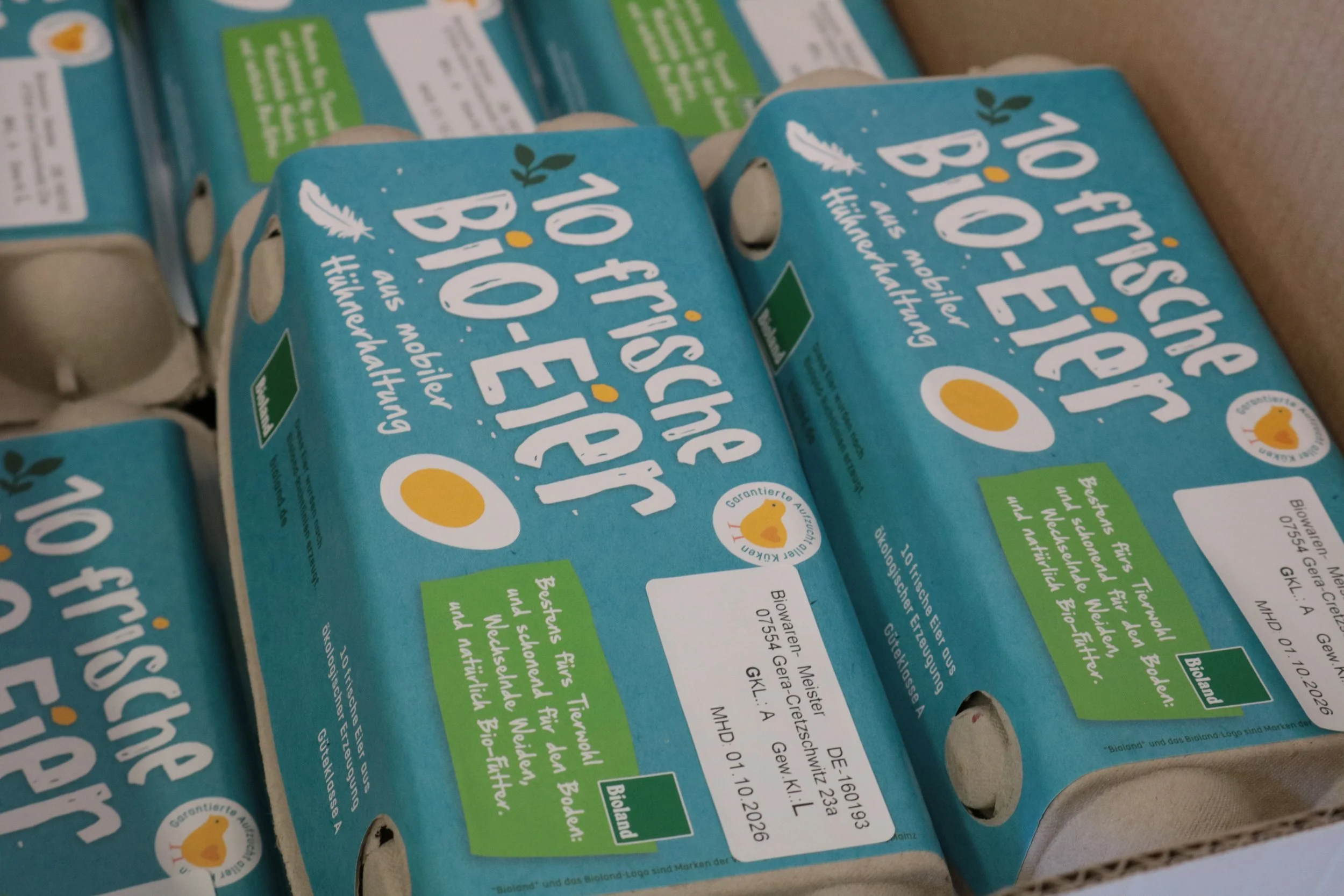 Close-up of multiple cartons of organic eggs with blue packaging, white and yellow text, and a small duck logo.