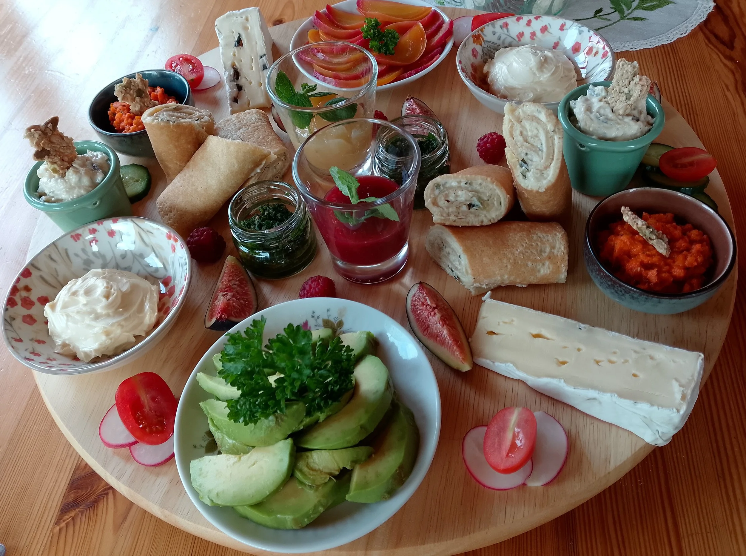 Assorted cheeses, fresh sliced tomatoes and cucumbers, raspberry, and various dips with bread and crackers on a wooden table.