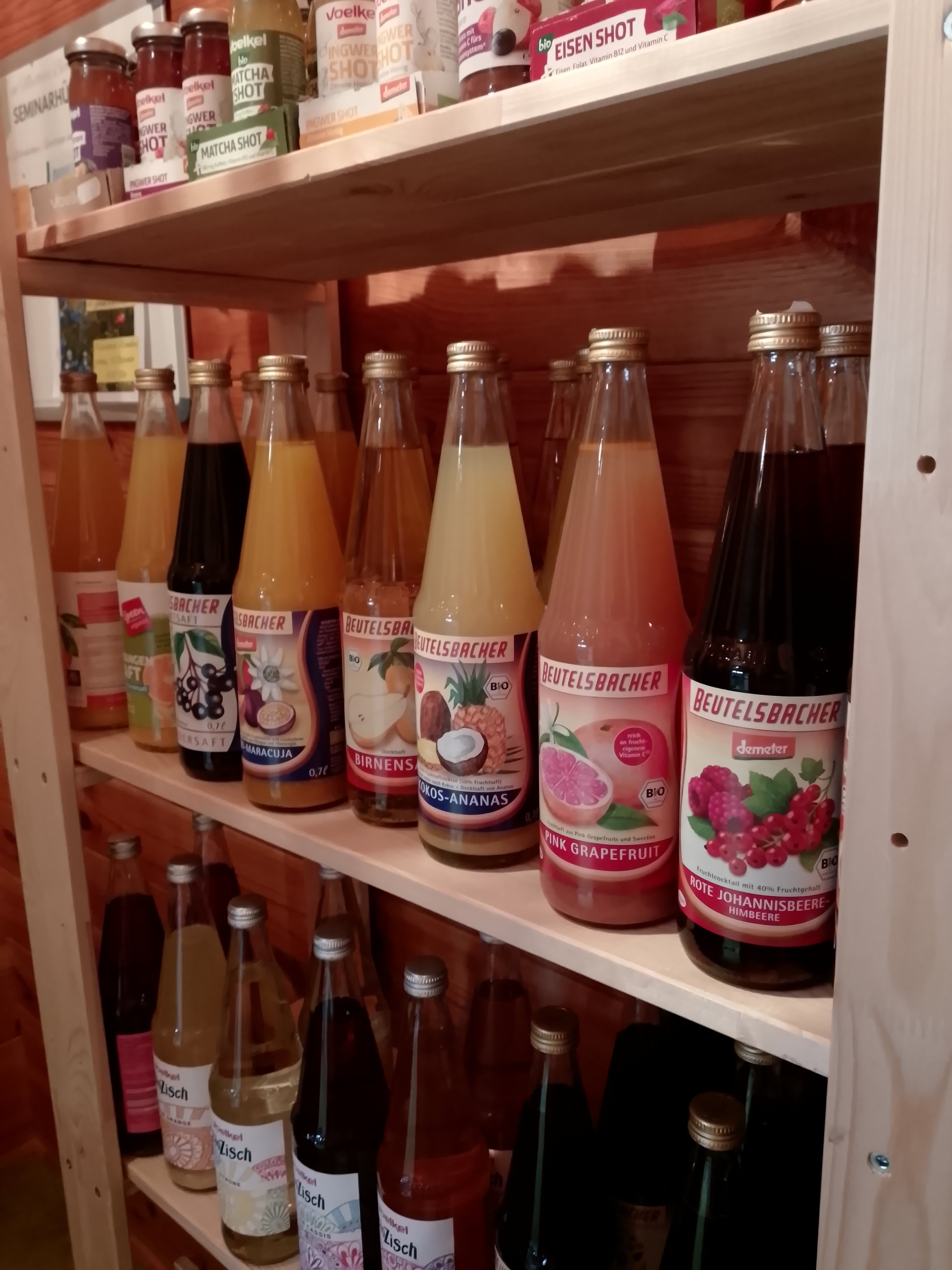 Shelf with bottles of fruit and vegetable juices, including flavors like pink grapefruit, black currant, pineapple, coconut, and raspberry.