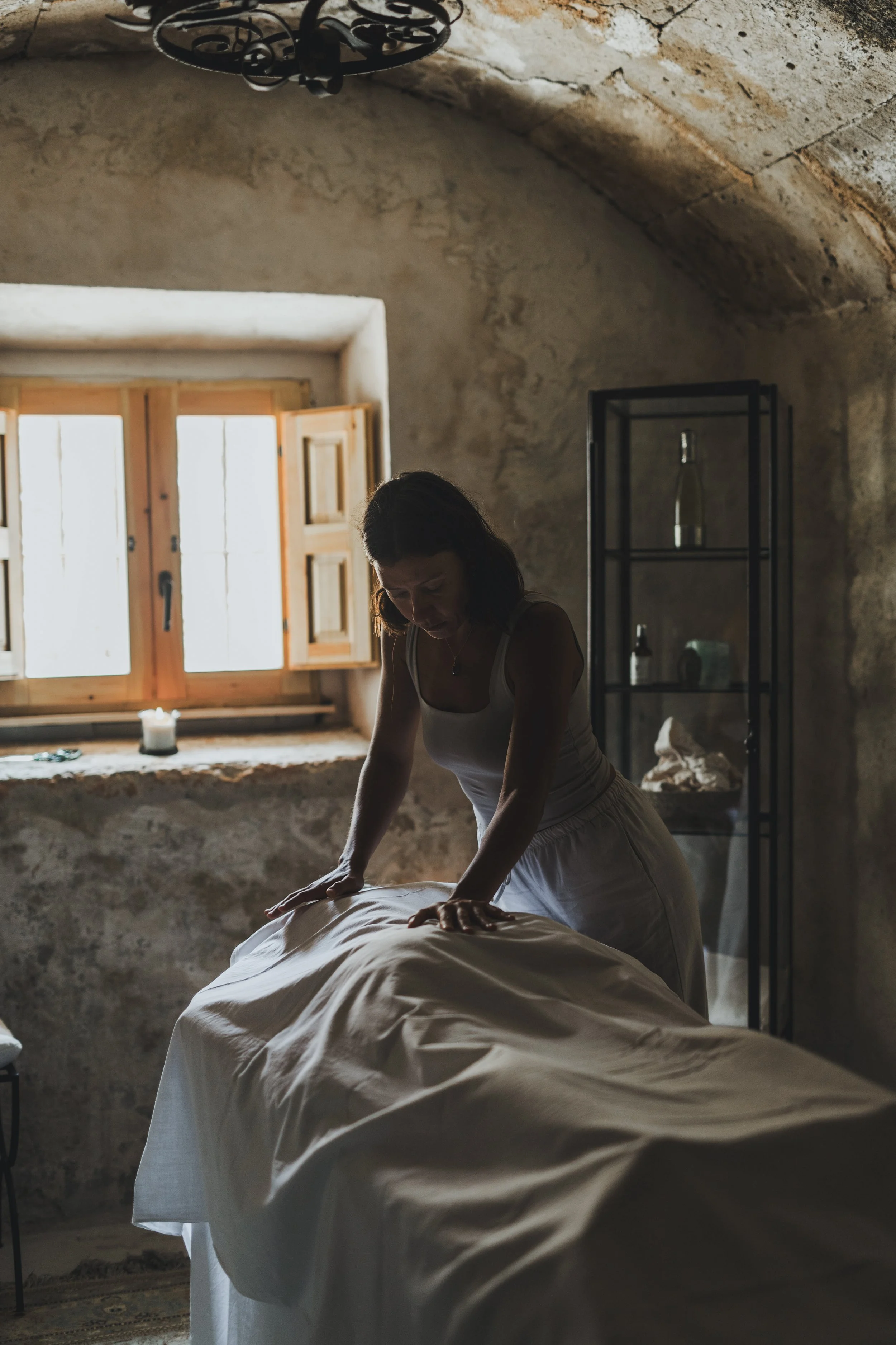 A woman giving a massage in a rustic room with stone walls and an open window.