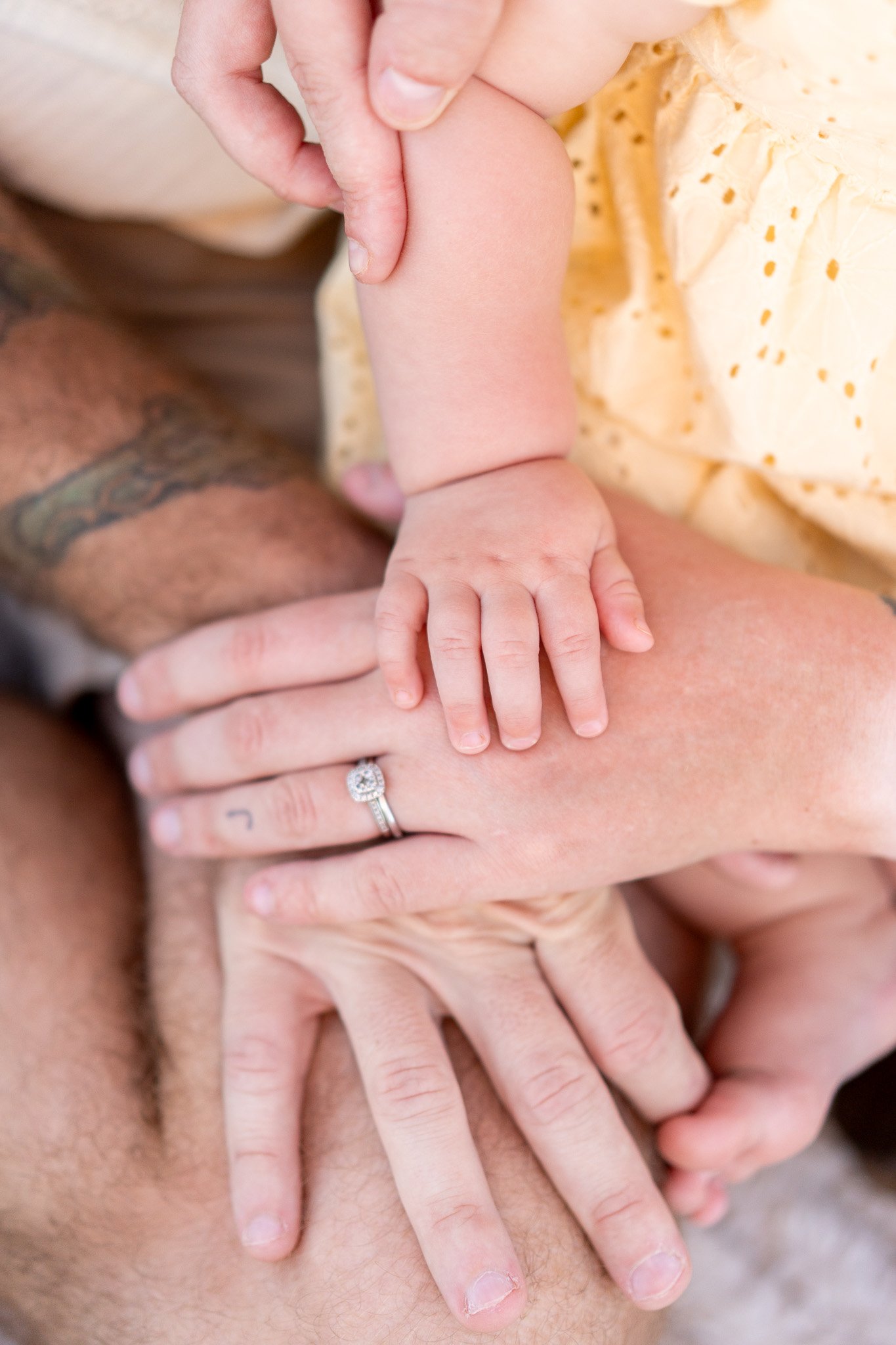 Close-up of a baby with parents' hands layered over the baby, showing them holding and supporting the baby.