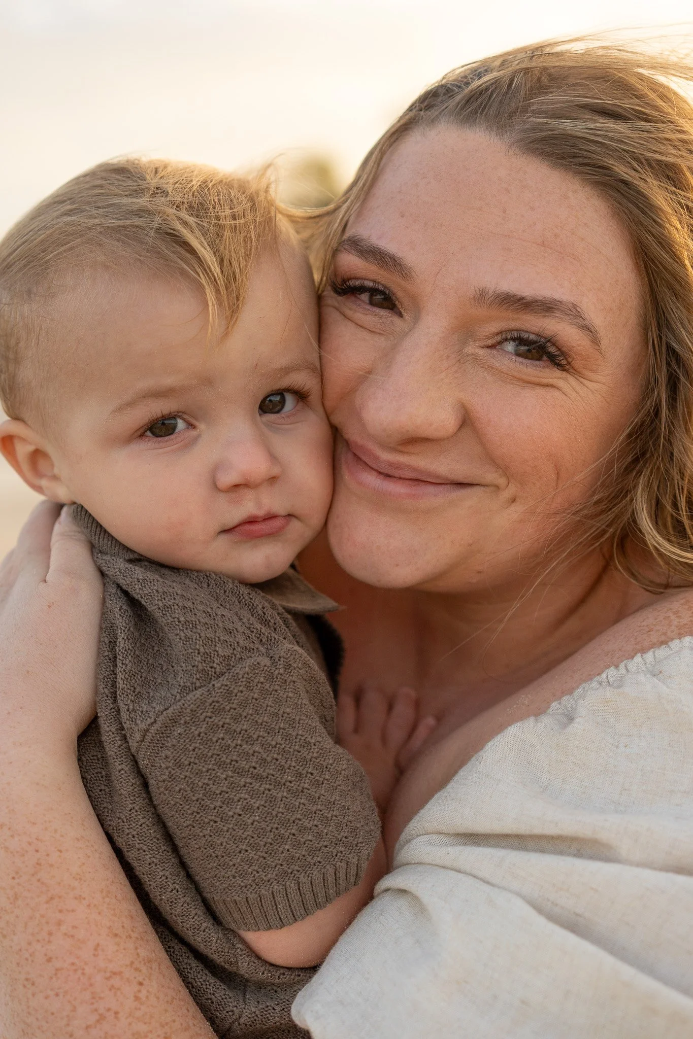 A woman and a young child are close together, smiling and cuddling during a sunny day.