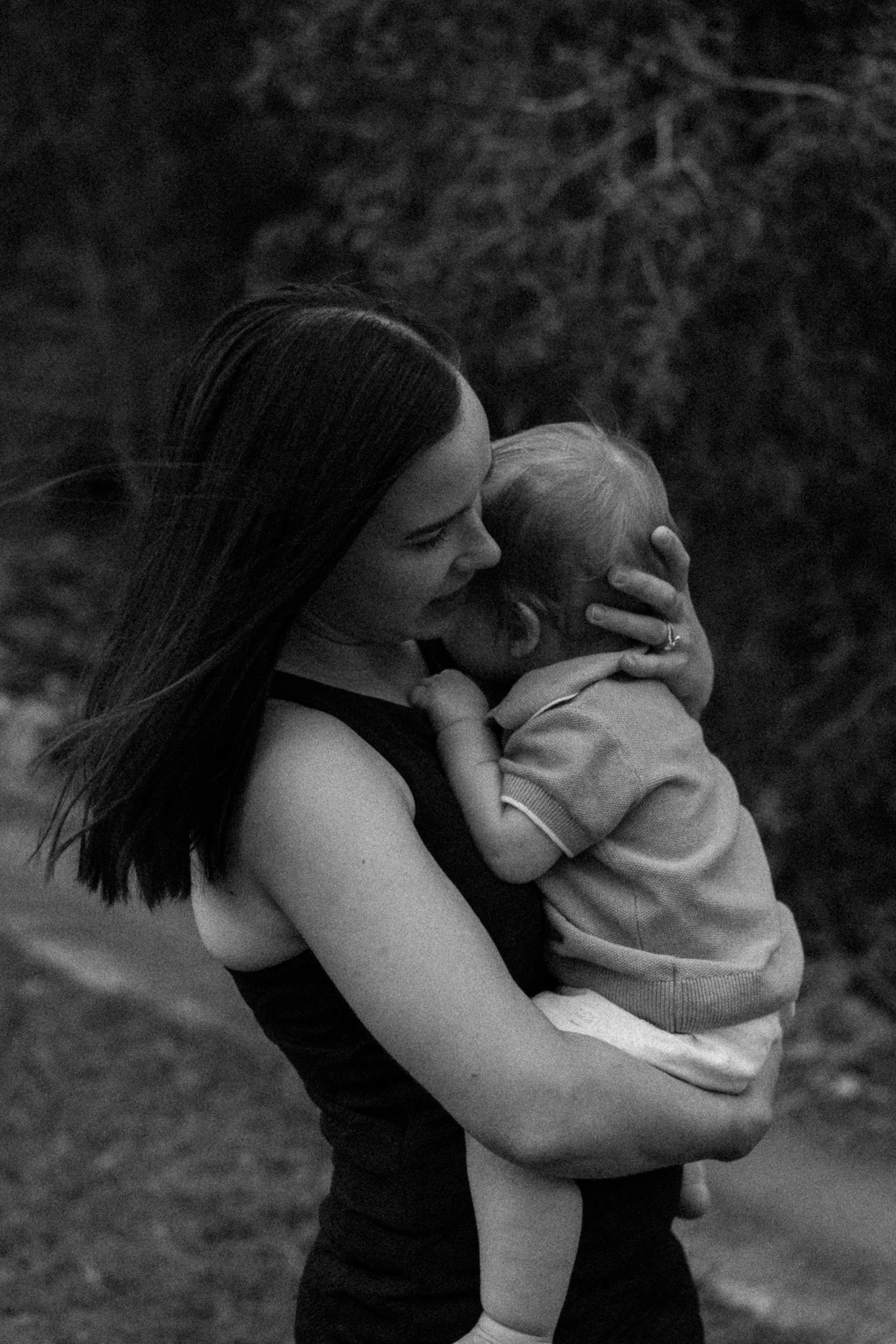A woman with long hair hugs a young child. They appear emotional and are outdoors with a blurred natural background.