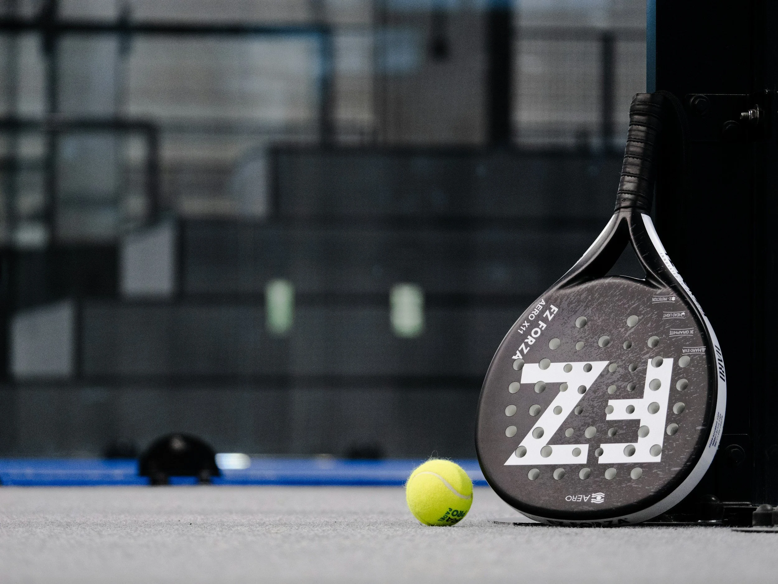 A tennis racket and two tennis balls on a court with a blurred background.