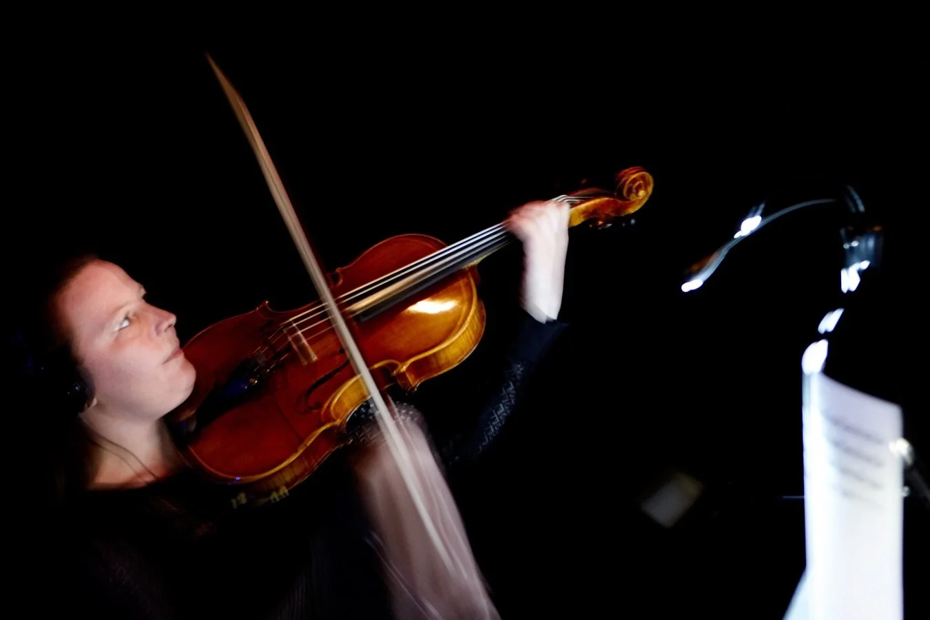 Woman playing violin in a recording studio with dark background.