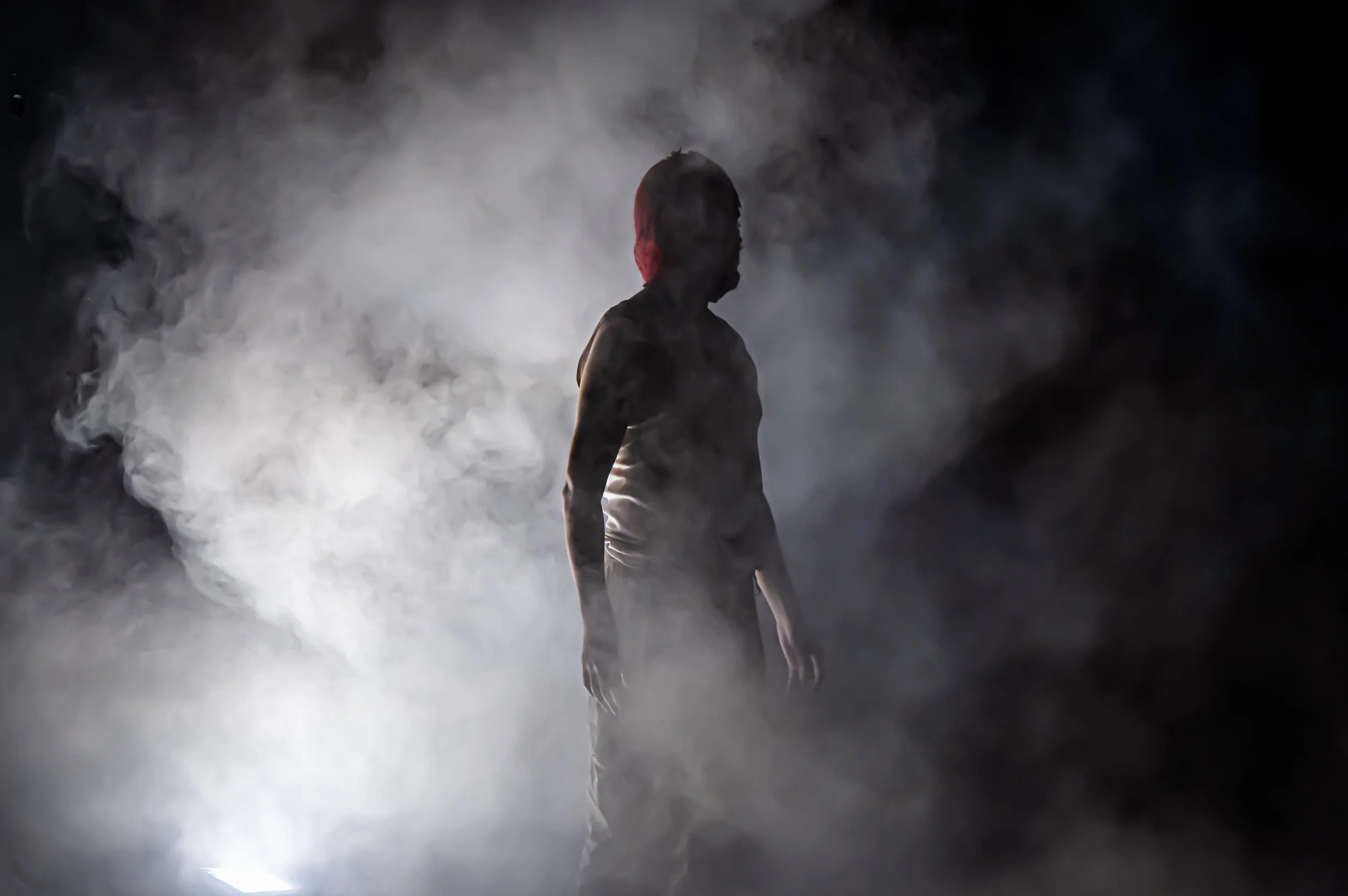 Silhouette of a person with a red hood standing amidst thick white smoke or fog, dark background.