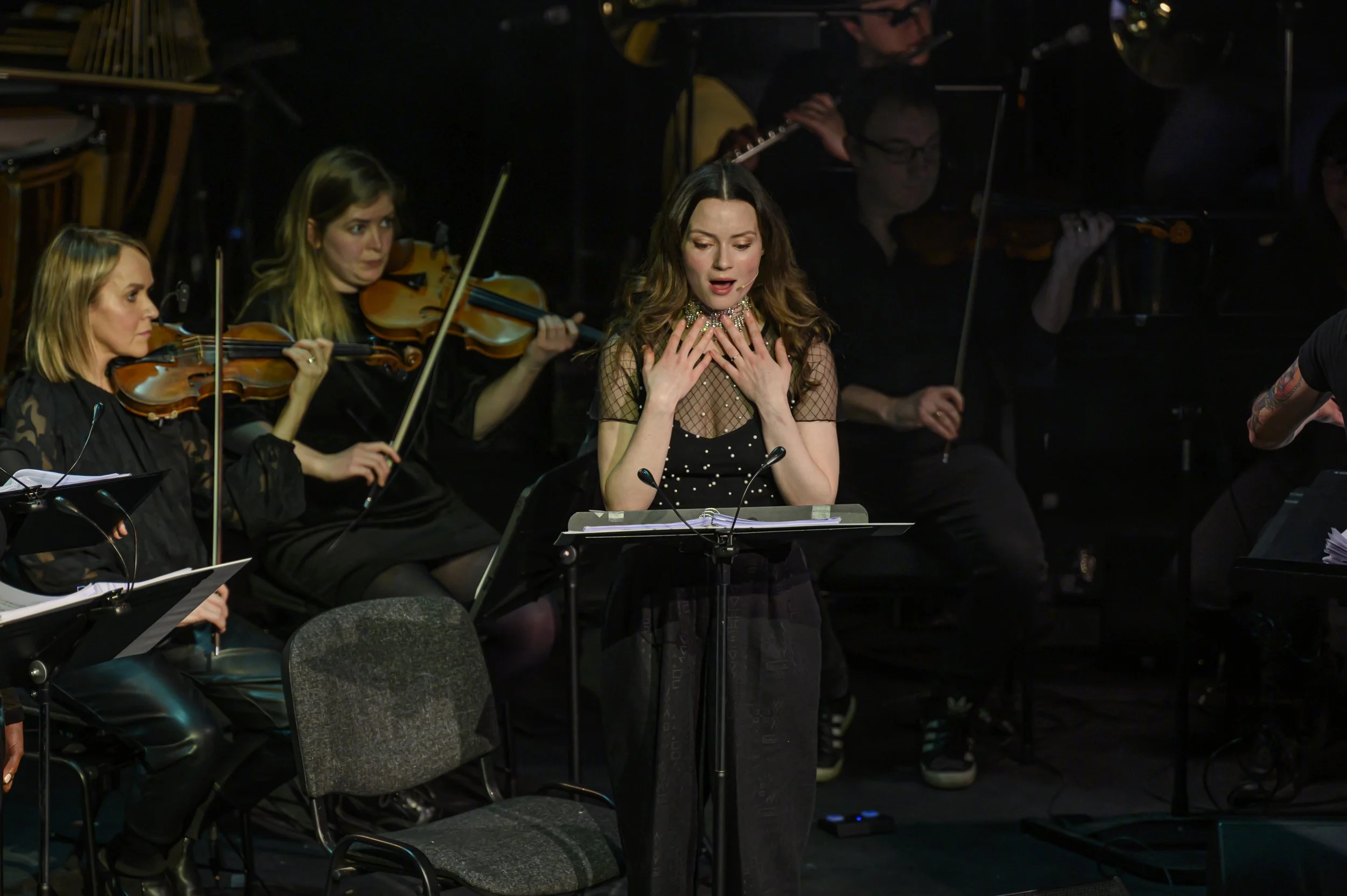 A woman singing at a microphone with an orchestra of string musicians behind her on stage.