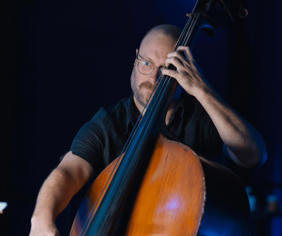 A man with glasses playing an upright bass in a dimly lit setting.