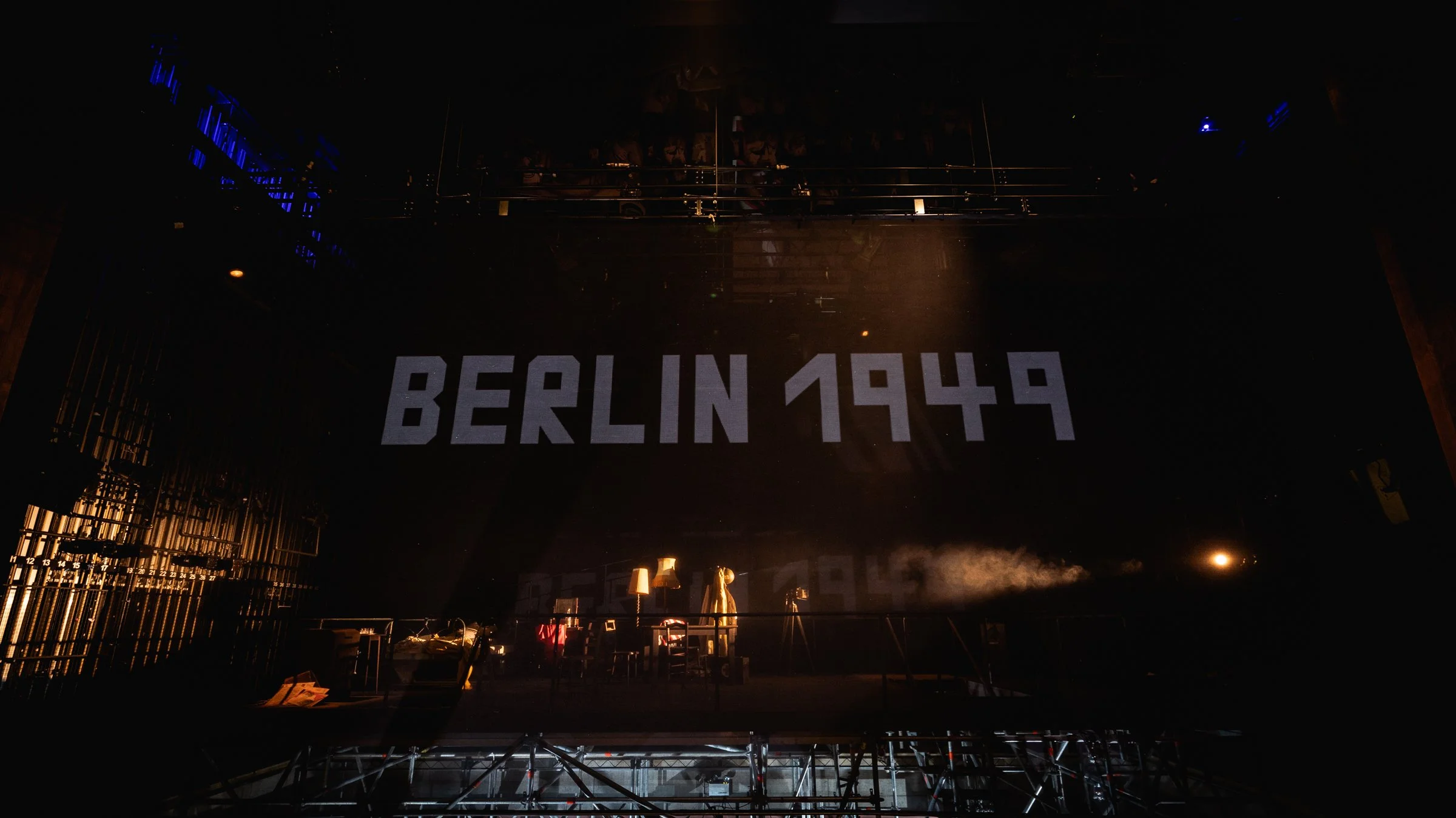 A large sign with the words 'BERLIN 1949' displayed prominently, illuminated in a dark setting with some stage or event equipment visible underneath.