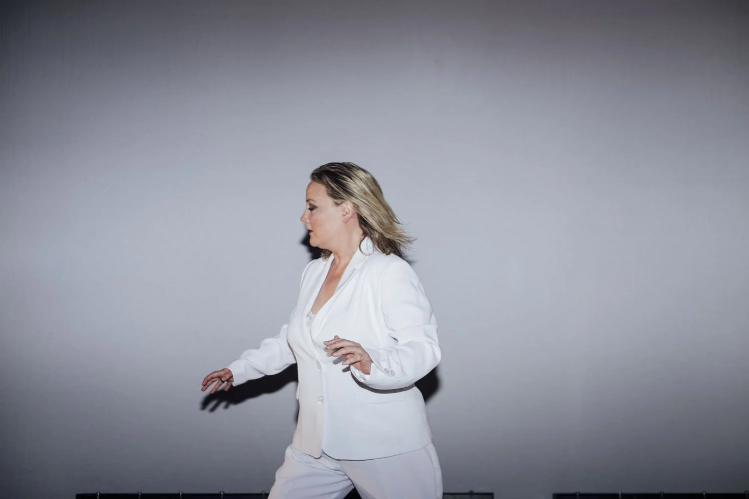 Woman in white suit dancing against a gray background.