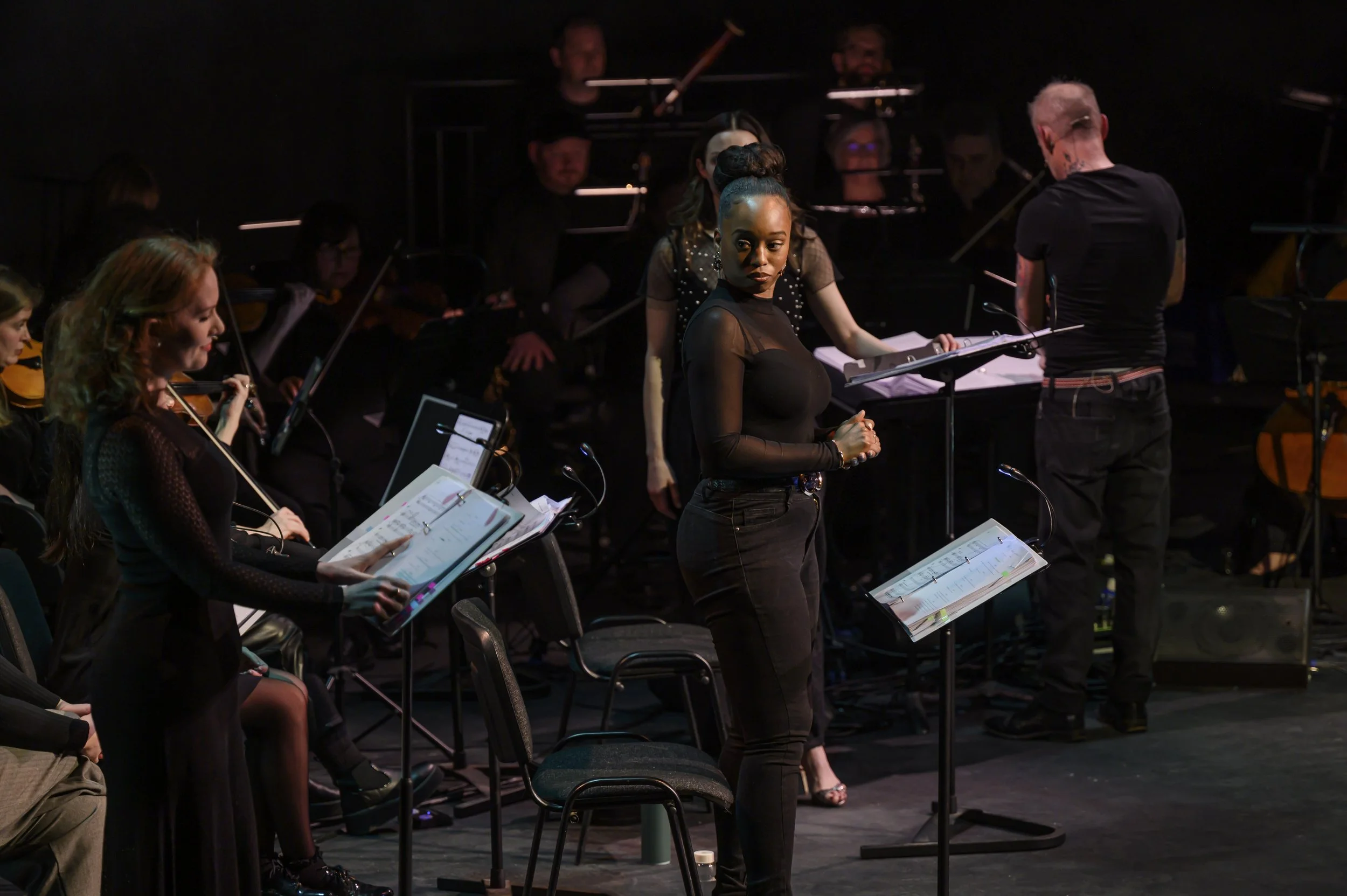 A woman standing in front of an orchestra practicing her singing.