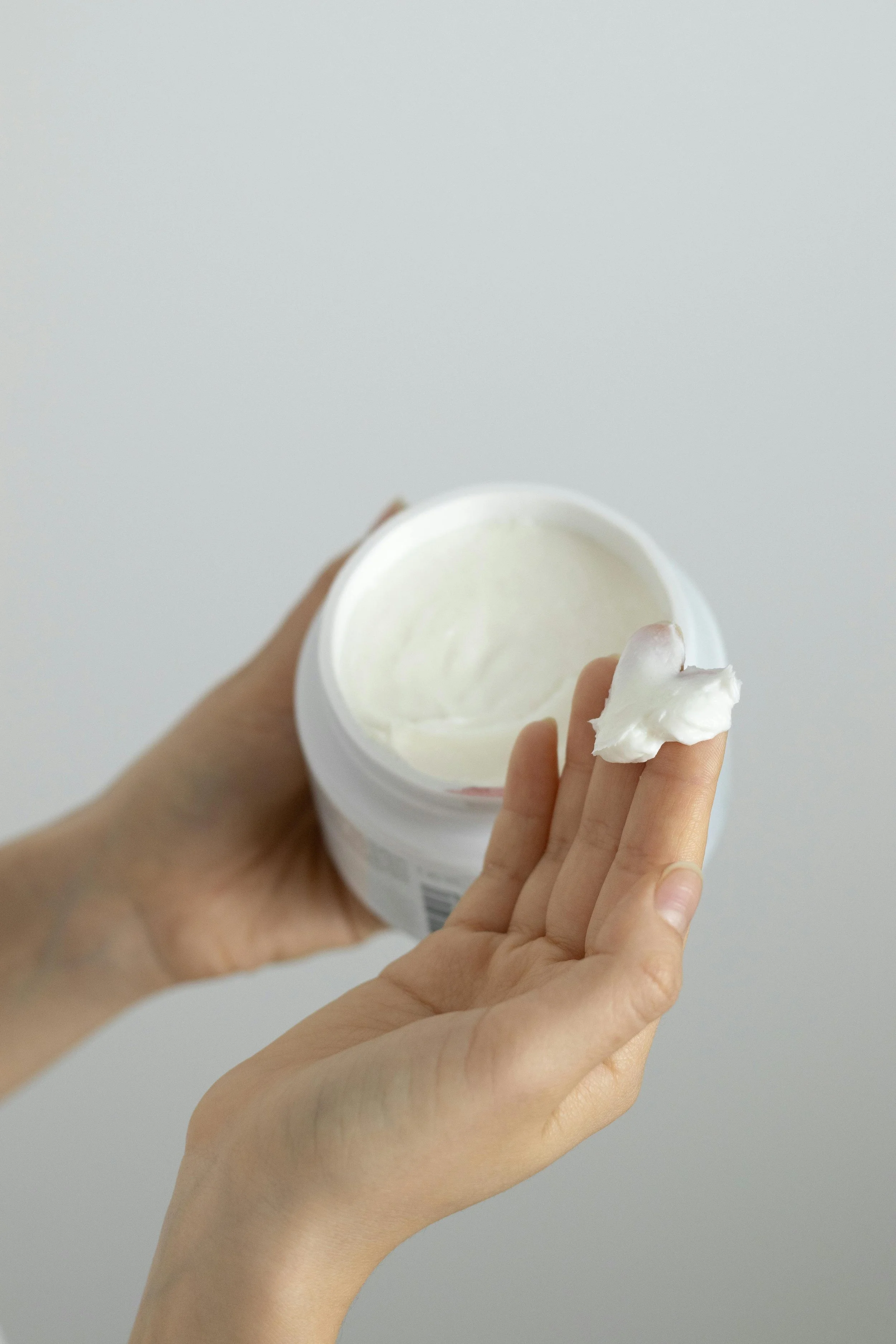 Person holding a white container of cream or lotion and a small amount of cream on their finger.